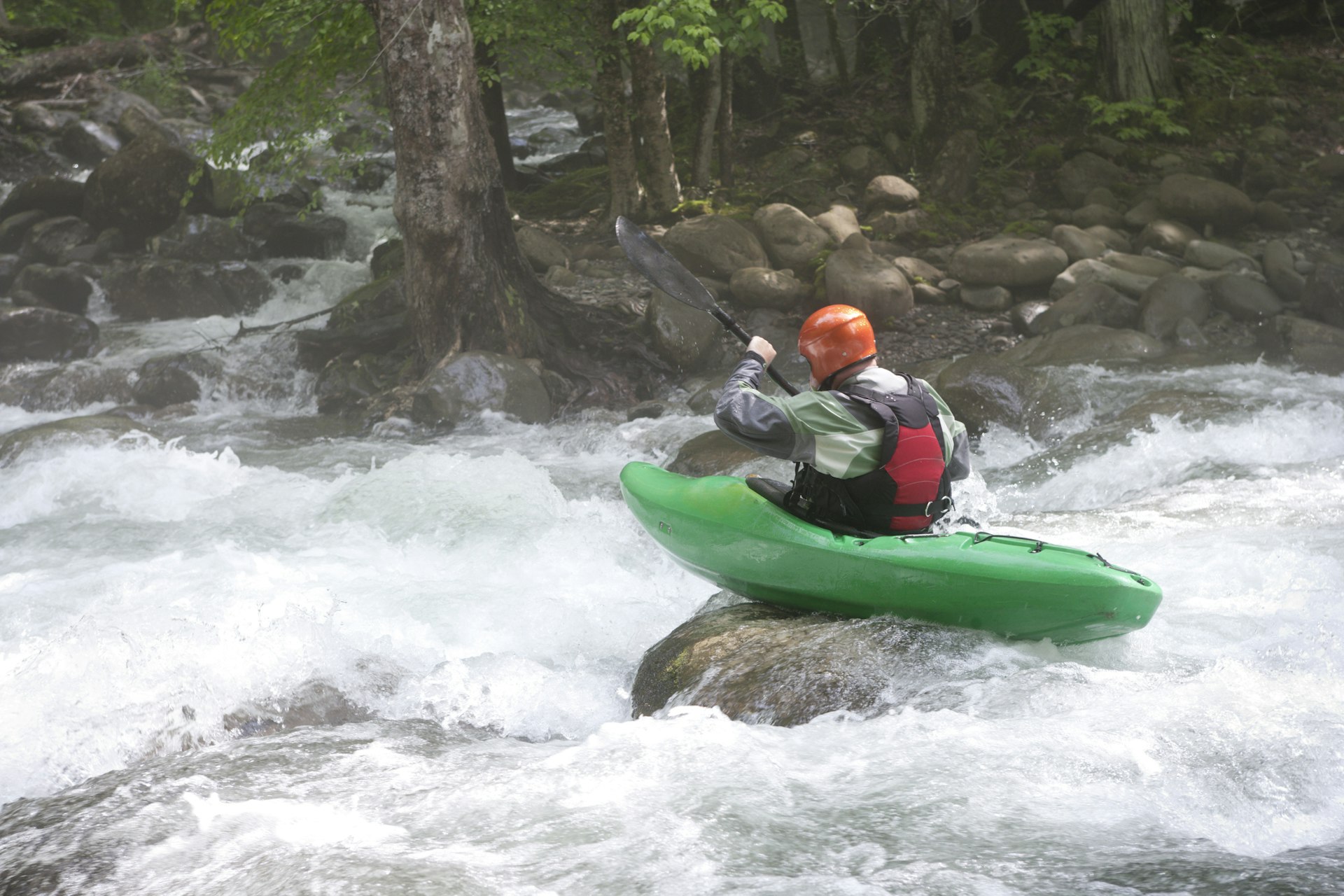 A kayaker on a rock prepares to head down some white water rapids in a fast-flowing creek