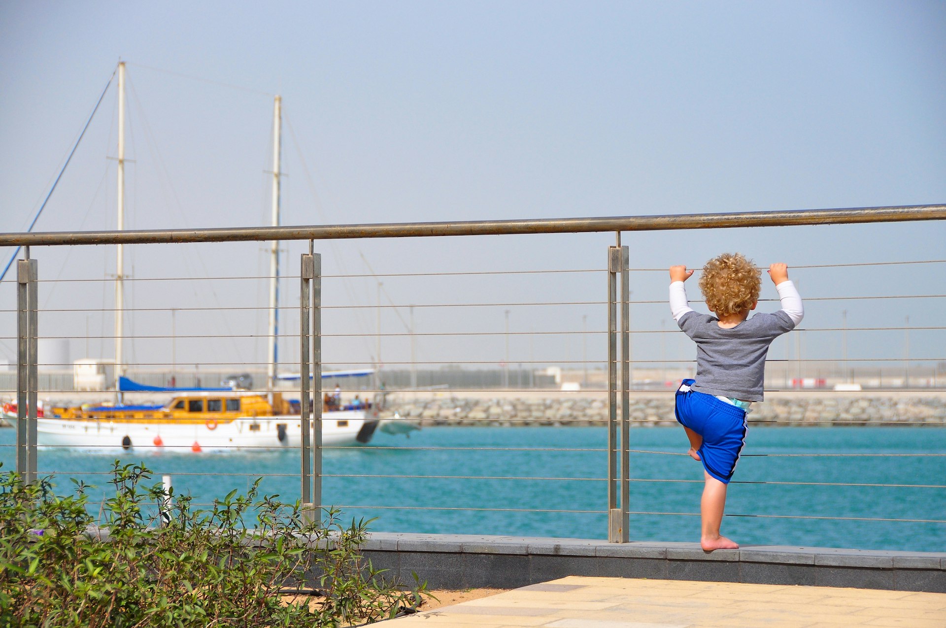 A young boy climbing the fence at Al Zeina residential complex, Abu Dhabi, overlooking the channel that separates Yas Island.