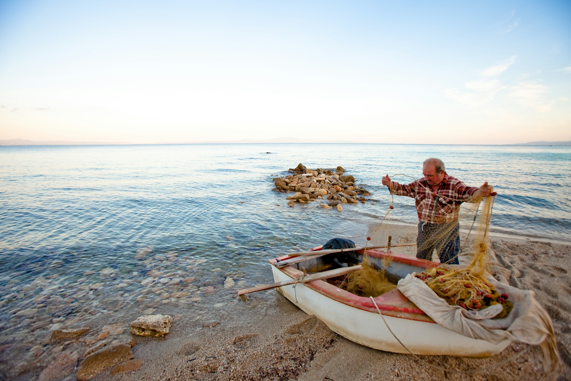 An old Greek fisherman rowing out from shore along the east coast of Northern Greece, in a small fishing village south of Thessaloniki. 