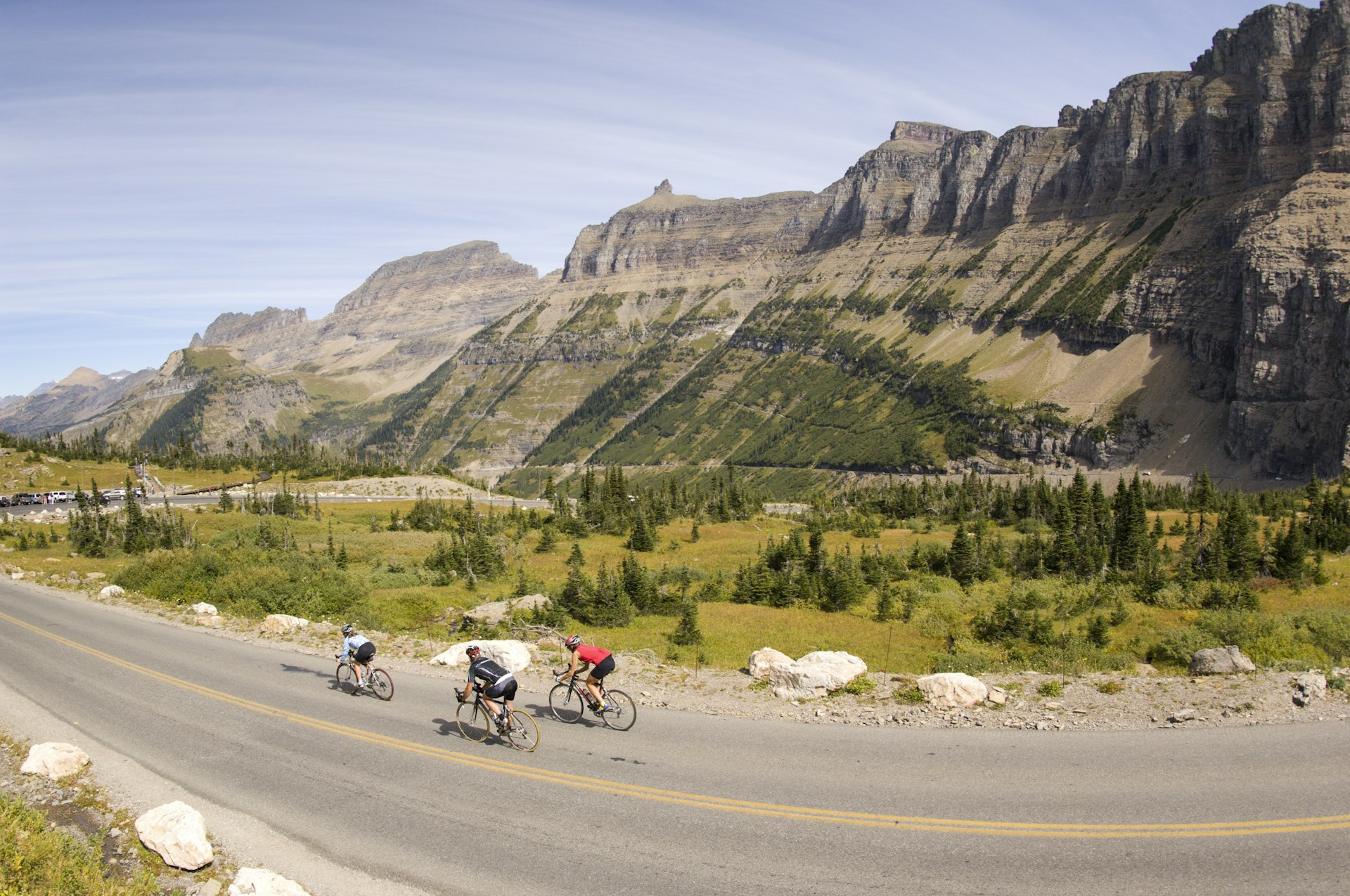 Three cyclists whizzing past rocky mountains in Glacier National Park, Montana