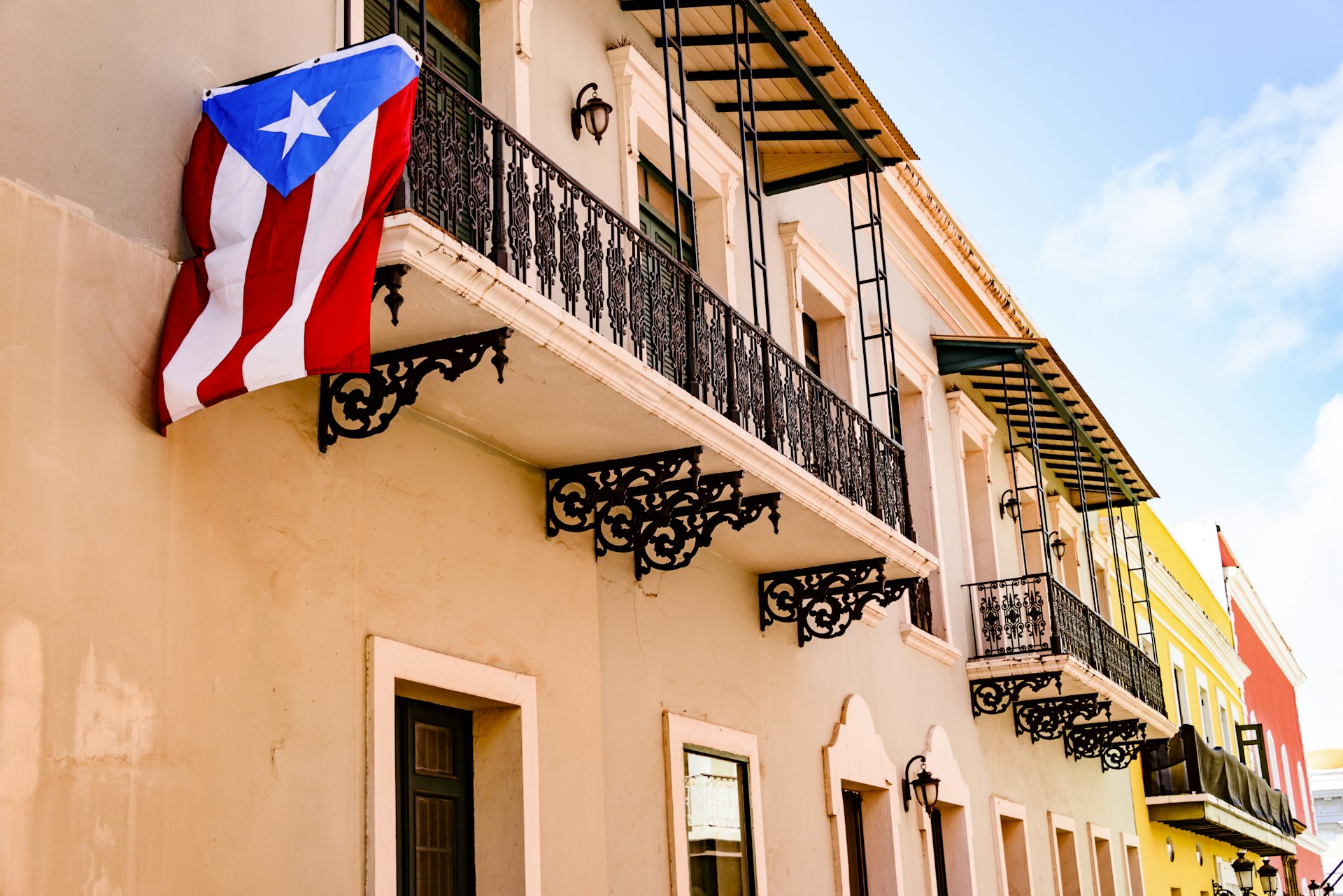 Colorful house facades along a street in Old San Juan, Puerto Rico, with a Puerto Rican flag hanging down from one of the balconies 