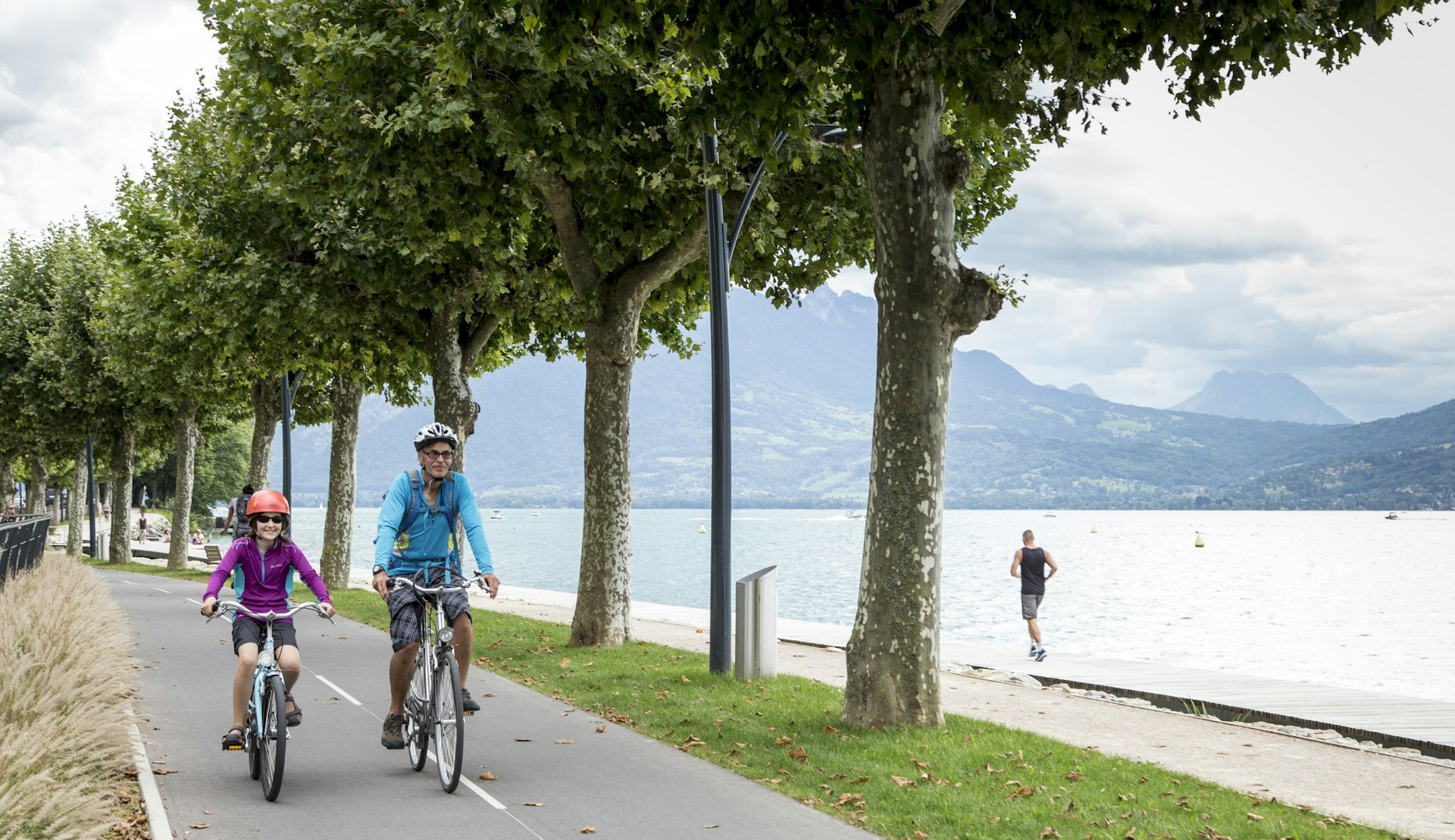 An adult and a child ride bikes alongside each other on a lakeside cycle path