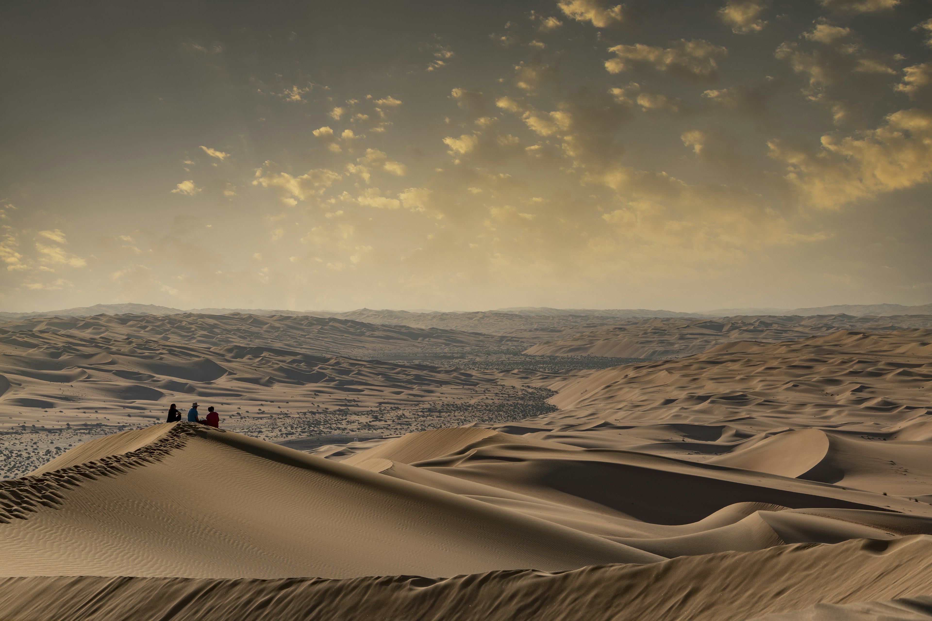 A family sitting on the top of a giant sand dune in the desert watching the sunset in the Empty Quarter, or Rub al Khali, the world's largest sand desert