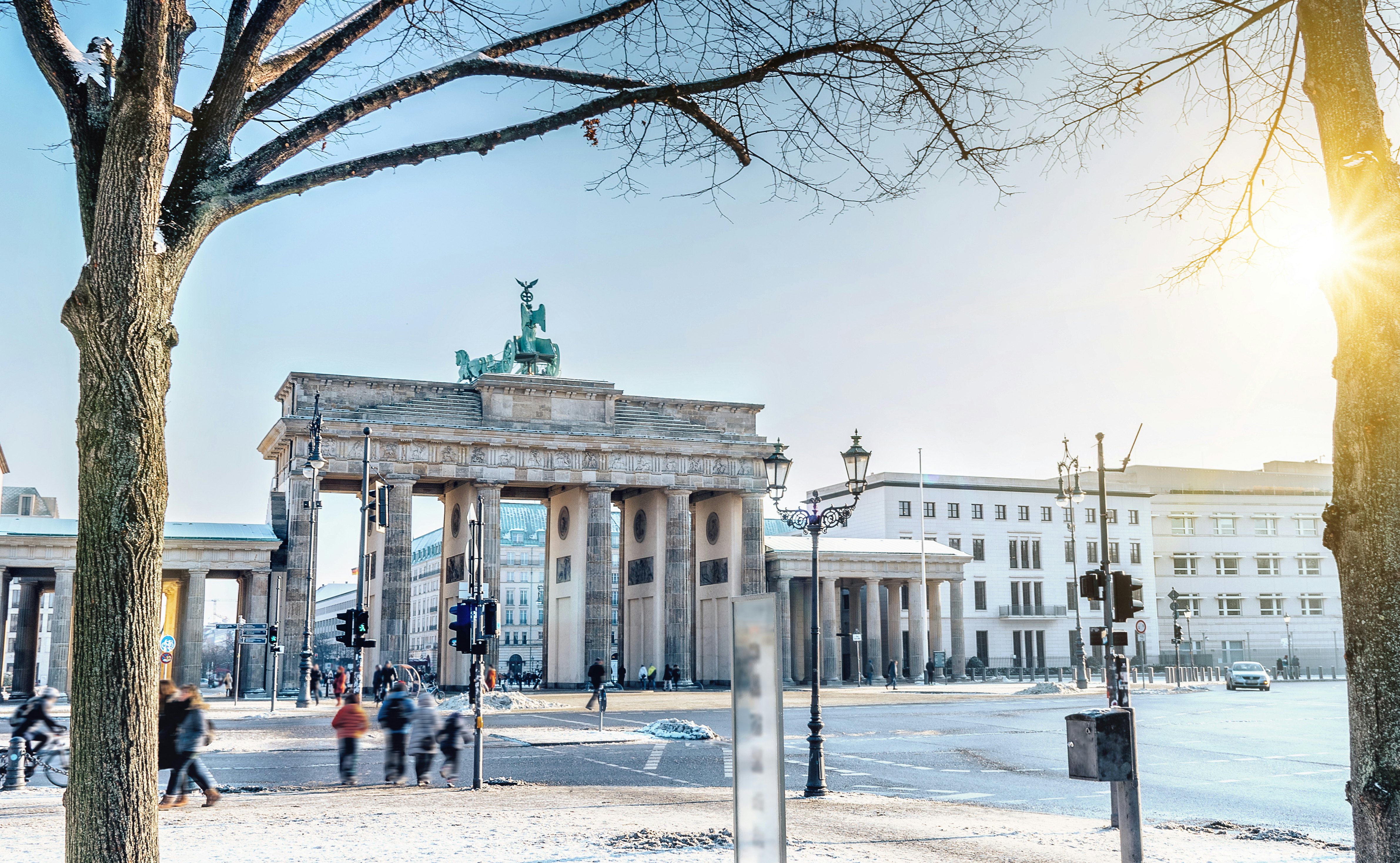 Out-of-focus people walk along a winter city street with a large stone gate along the roadway on a sunny day.