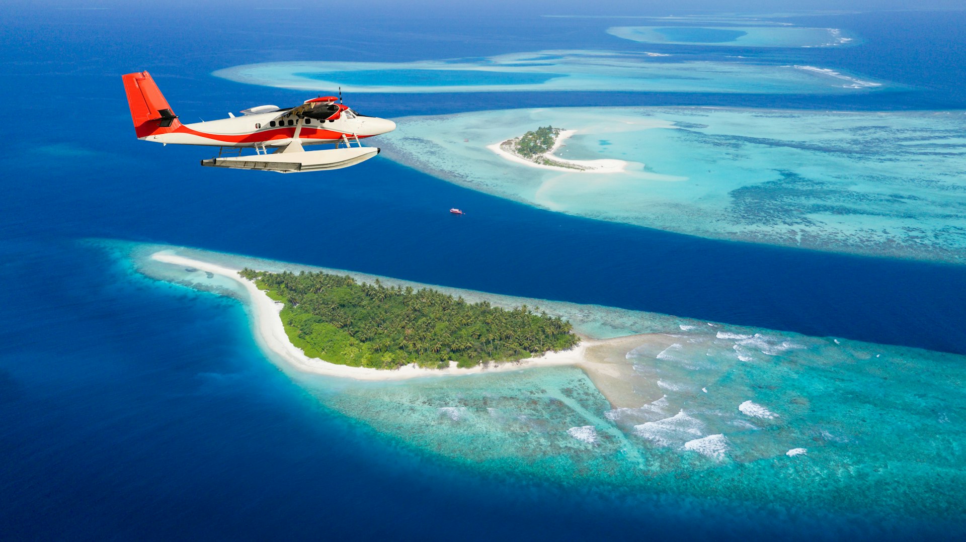 A seaplane glides through the sky above small islands and islets in the middle of a blue ocean