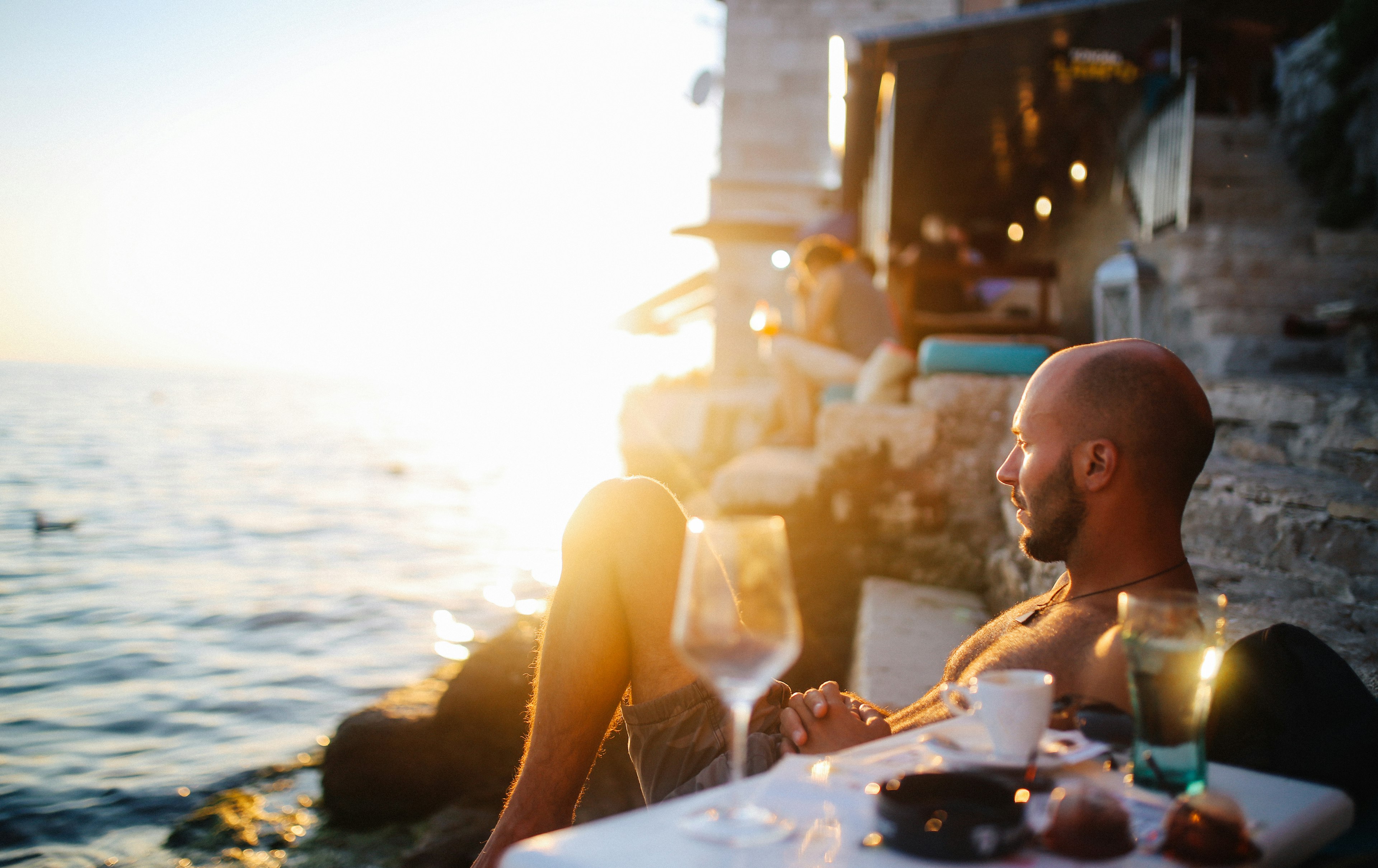 Portrait of a young man, sitting by the beach in an outdoors cafe in the Croatian seaside, Mediterranean. He is enjoying watching the sunset, having an espresso coffee in the dusk.