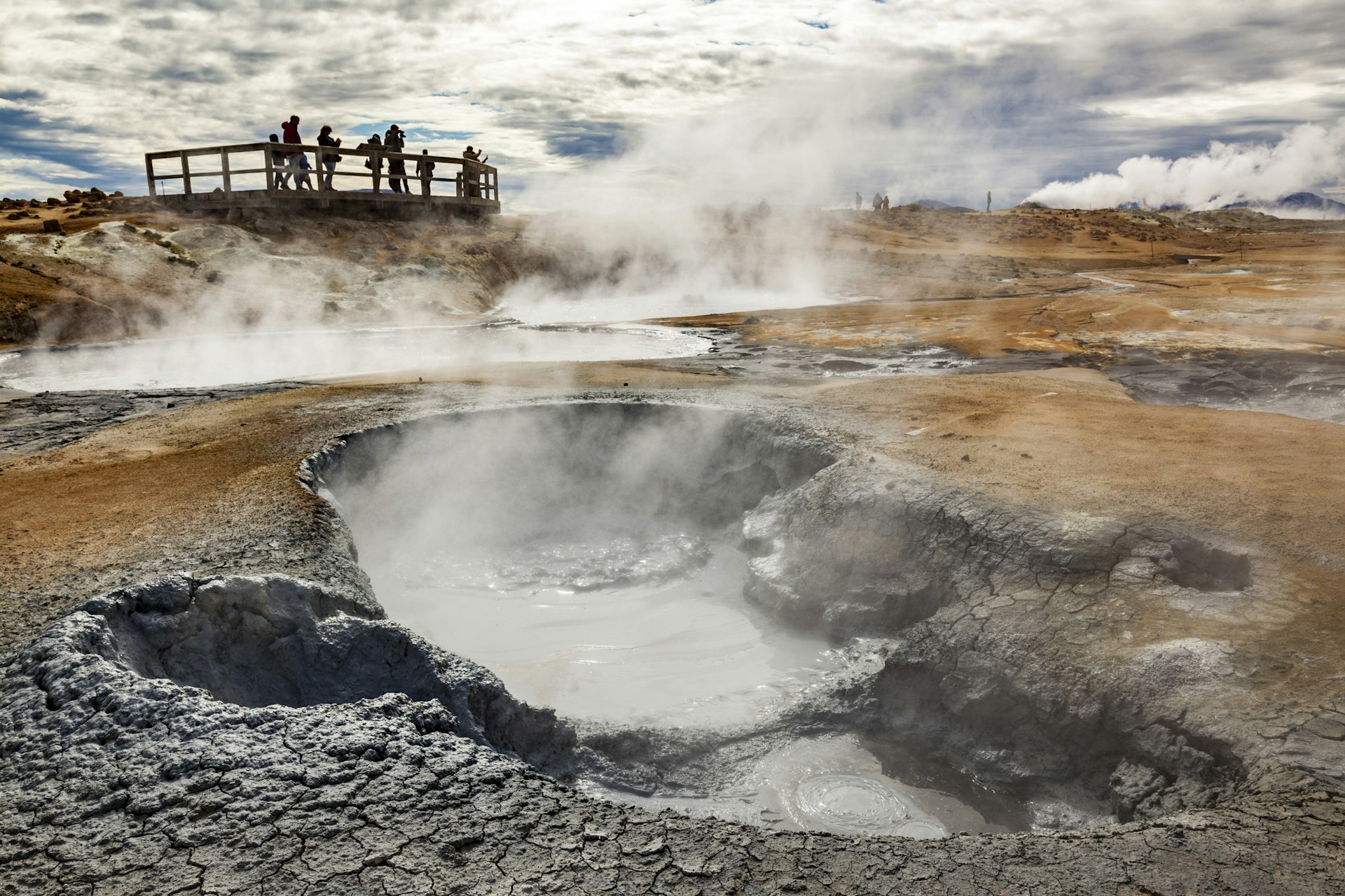 Visitors stand on a nearby viewing bridge to watch a bubbling mud pot roiling near the hydrothermal Lake Mývatn in Iceland