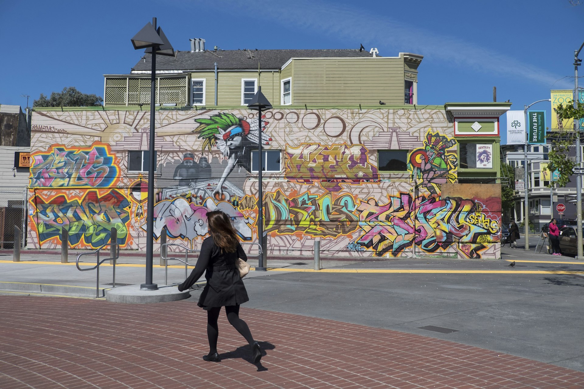 A woman in a black coat walks past a vibrant street mural in Bernal Heights, San Francisco.