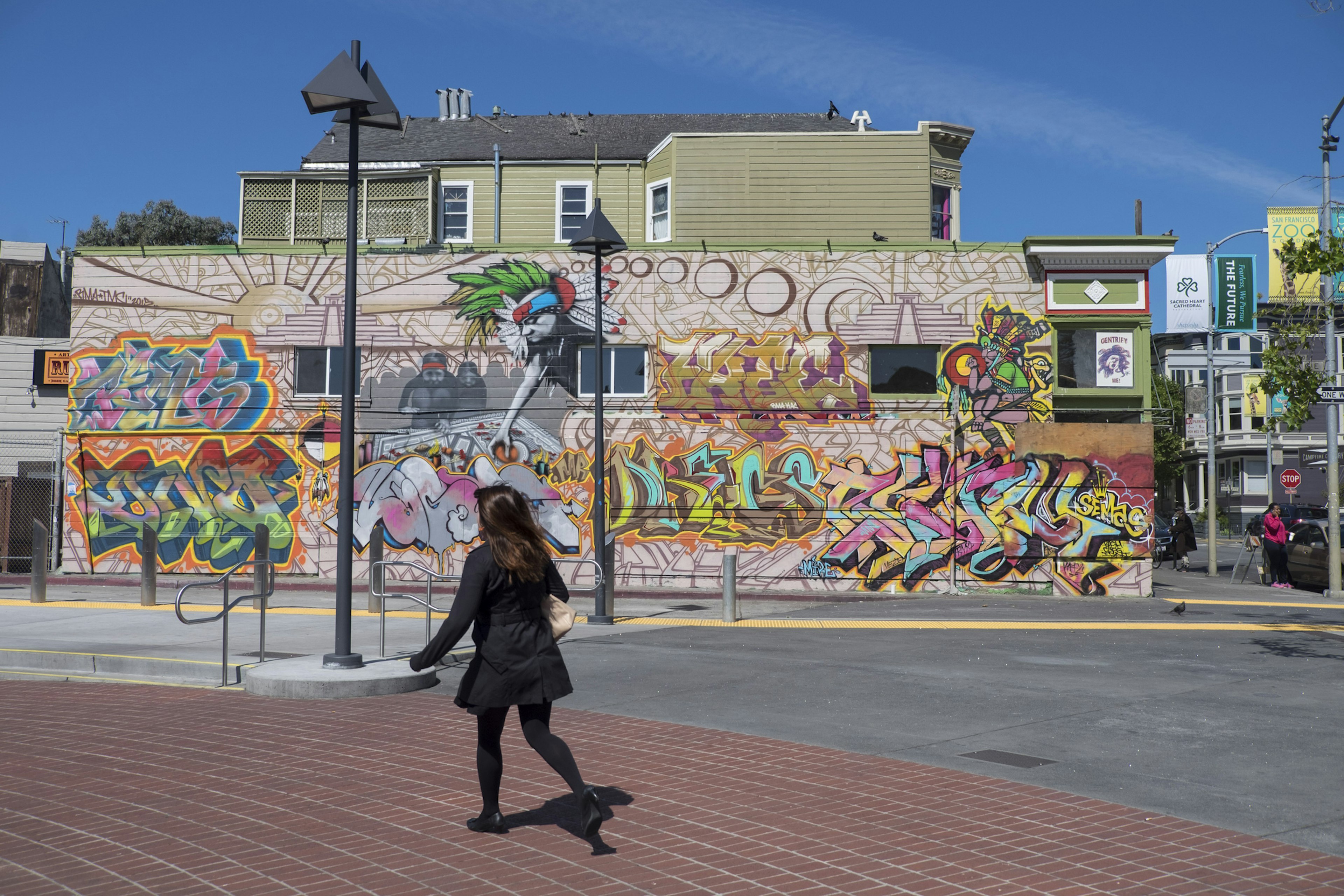 A woman in a black coat walks past a vibrant street mural in Bernal Heights, San Francisco.