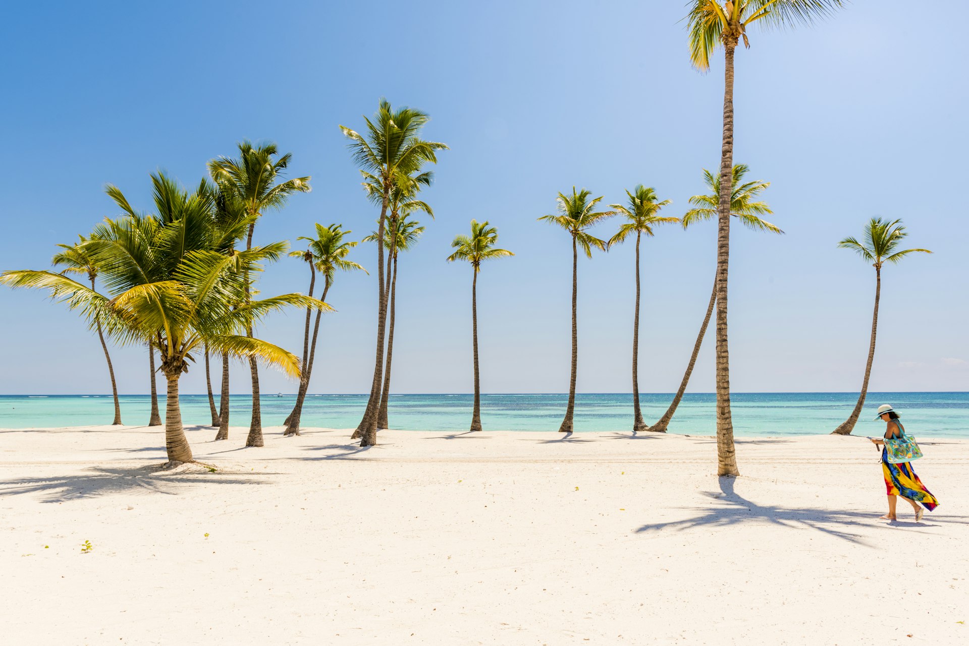 A woman walks on a gleaming white-sand beach that's dotted with palm trees at Punta Cana, Dominican Republic