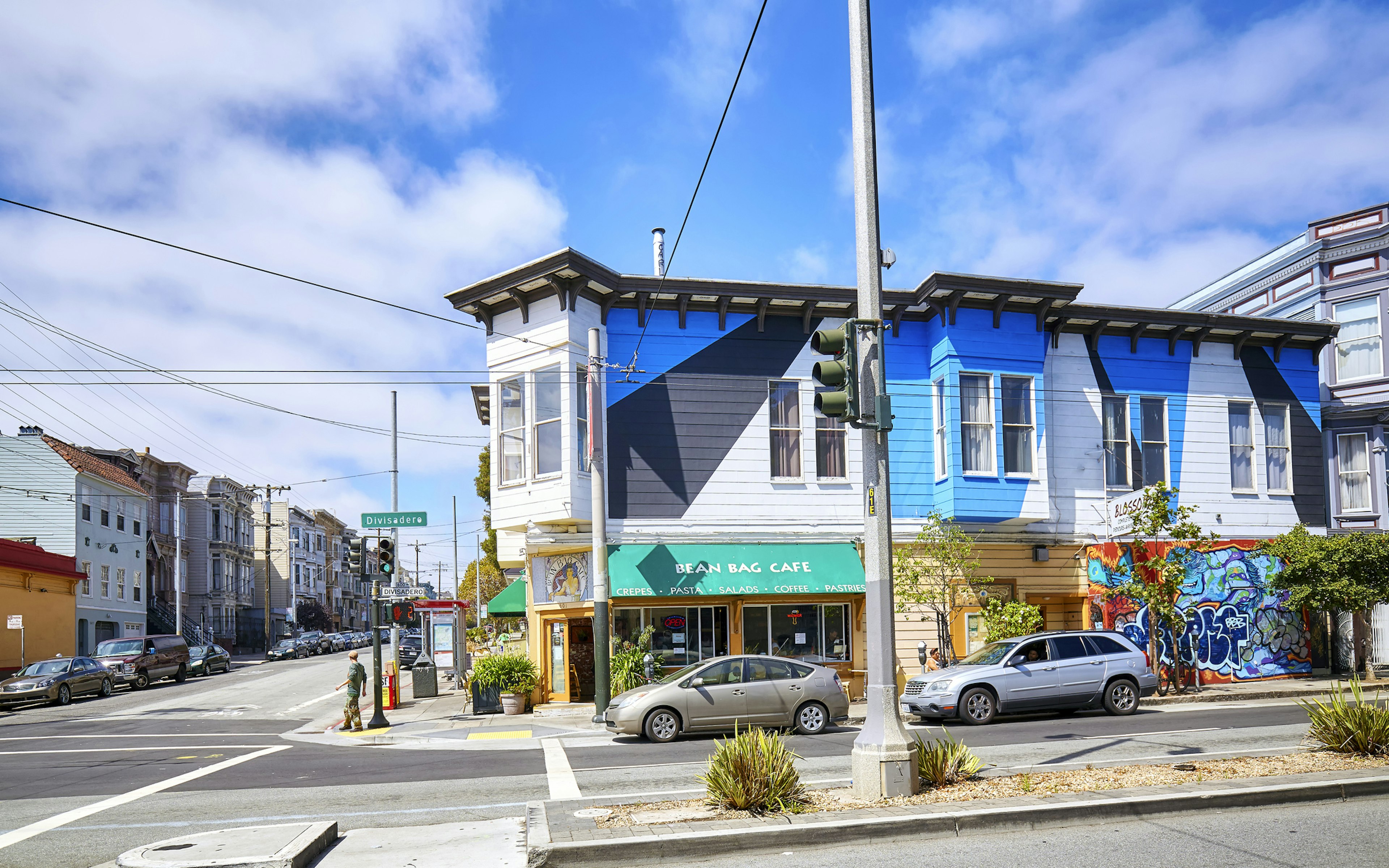 A street corner in San Francisco on a sunny day, with a two-story building painted in blue and white.