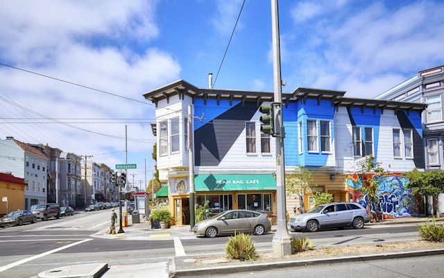 A street corner in San Francisco on a sunny day, with a two-story building painted in blue and white.