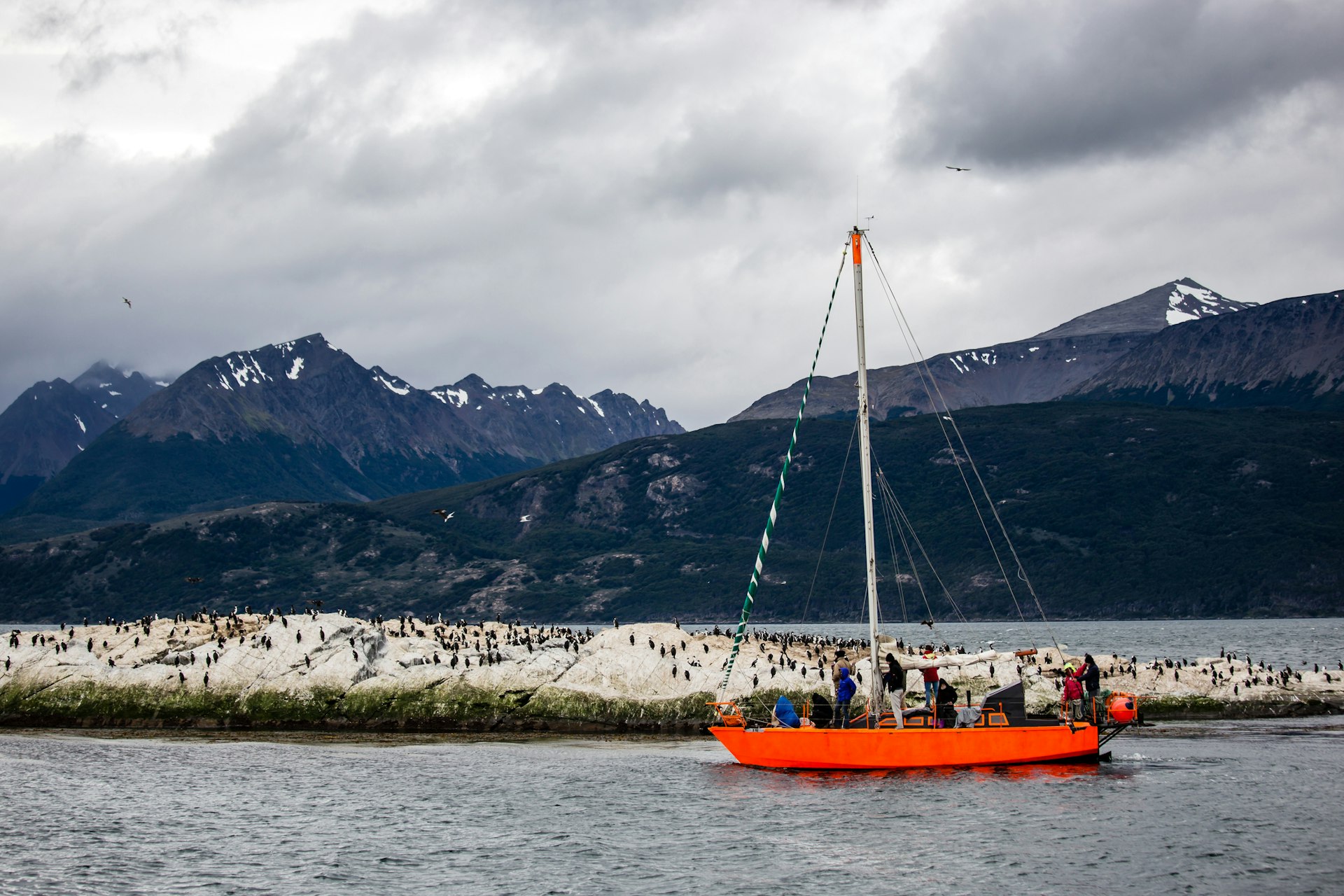 A bright orange sailboat visiting the Beagle Channel, with rocky islands inhabited by cormorants