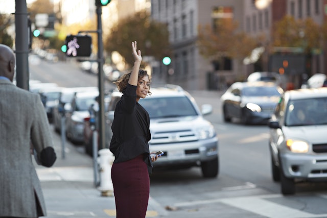 A young woman hails a taxi on a busy city street