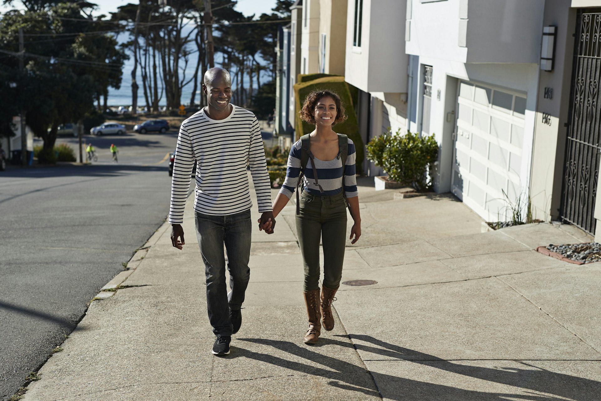 A smiling man and woman are walking hand in hand on a city sidewalk