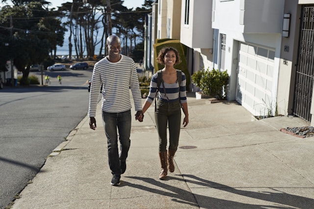 A smiling man and woman are walking hand in hand on a city sidewalk