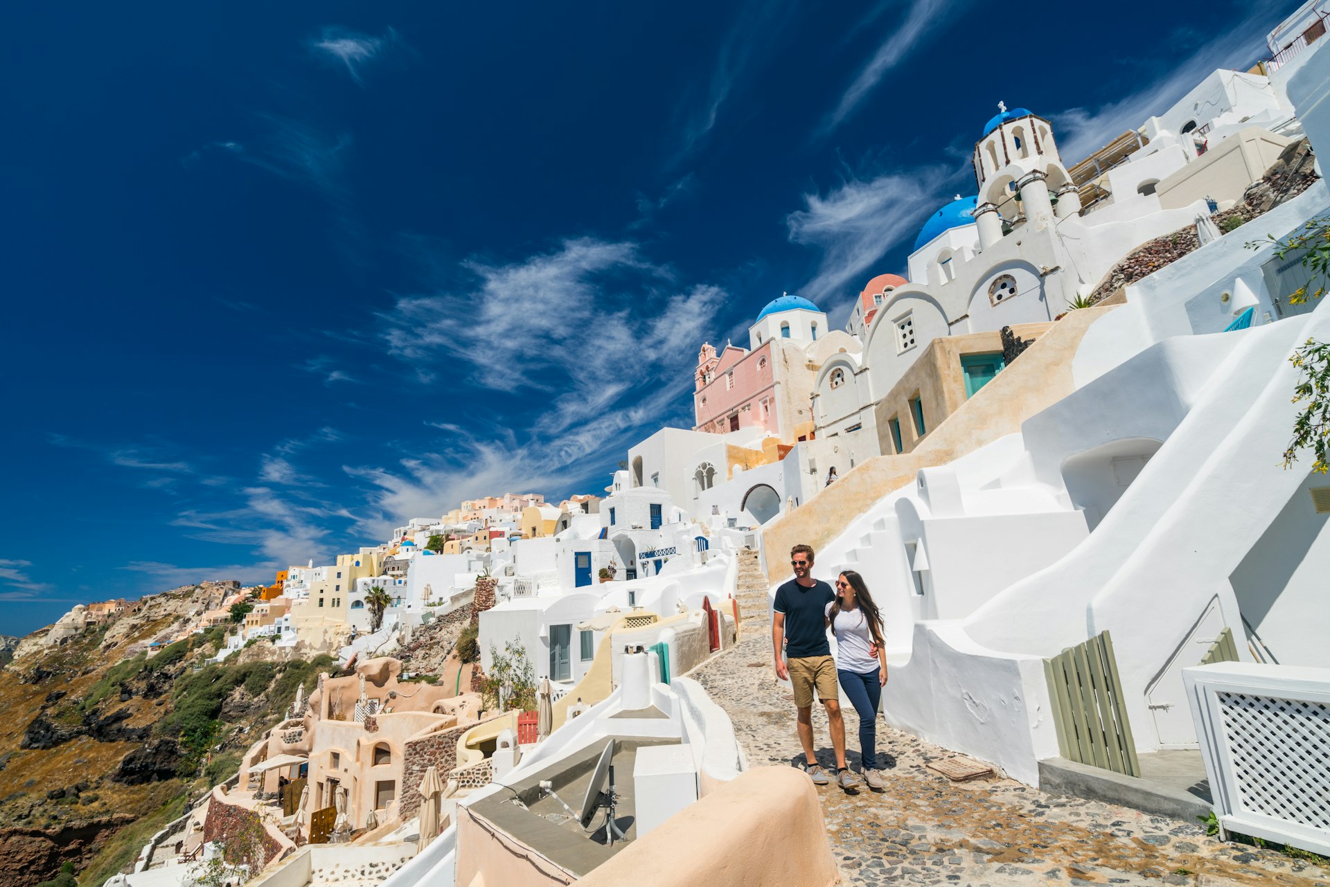 A couple walks among the iconic white buildings of Oia, Santorini, Cyclades, Greece