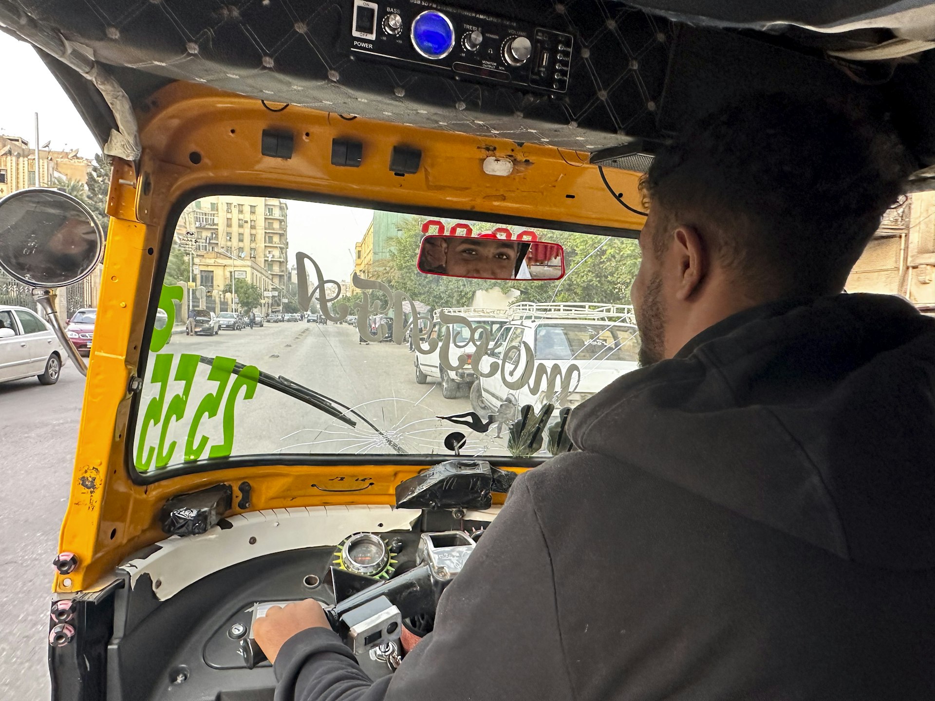 A tuk-tuk driver gives a small smile to his passenger in the rear-view mirror as he drives along