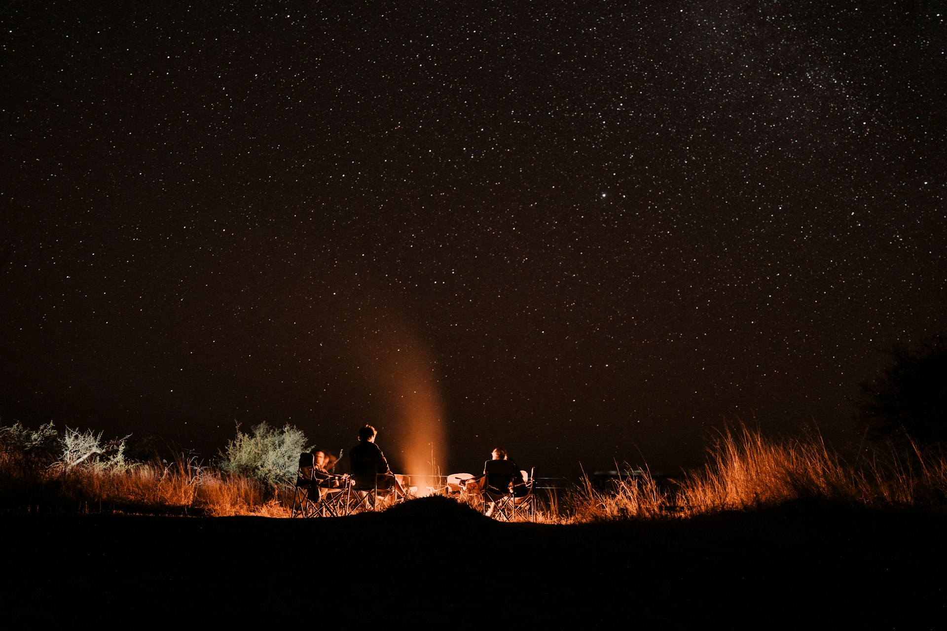 People gather around a campfire under a starry night sky in Botswana