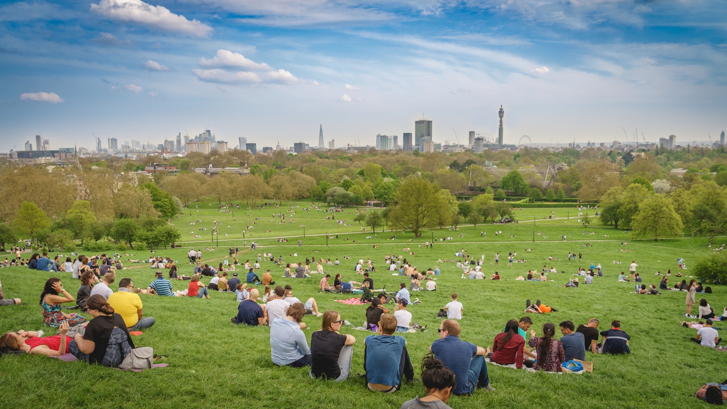 London, UK - April, 2018. Breath-taking panoramic scenic view of London cityscape seen from a crowded Primrose Hill park on a sunny spring afternoon.