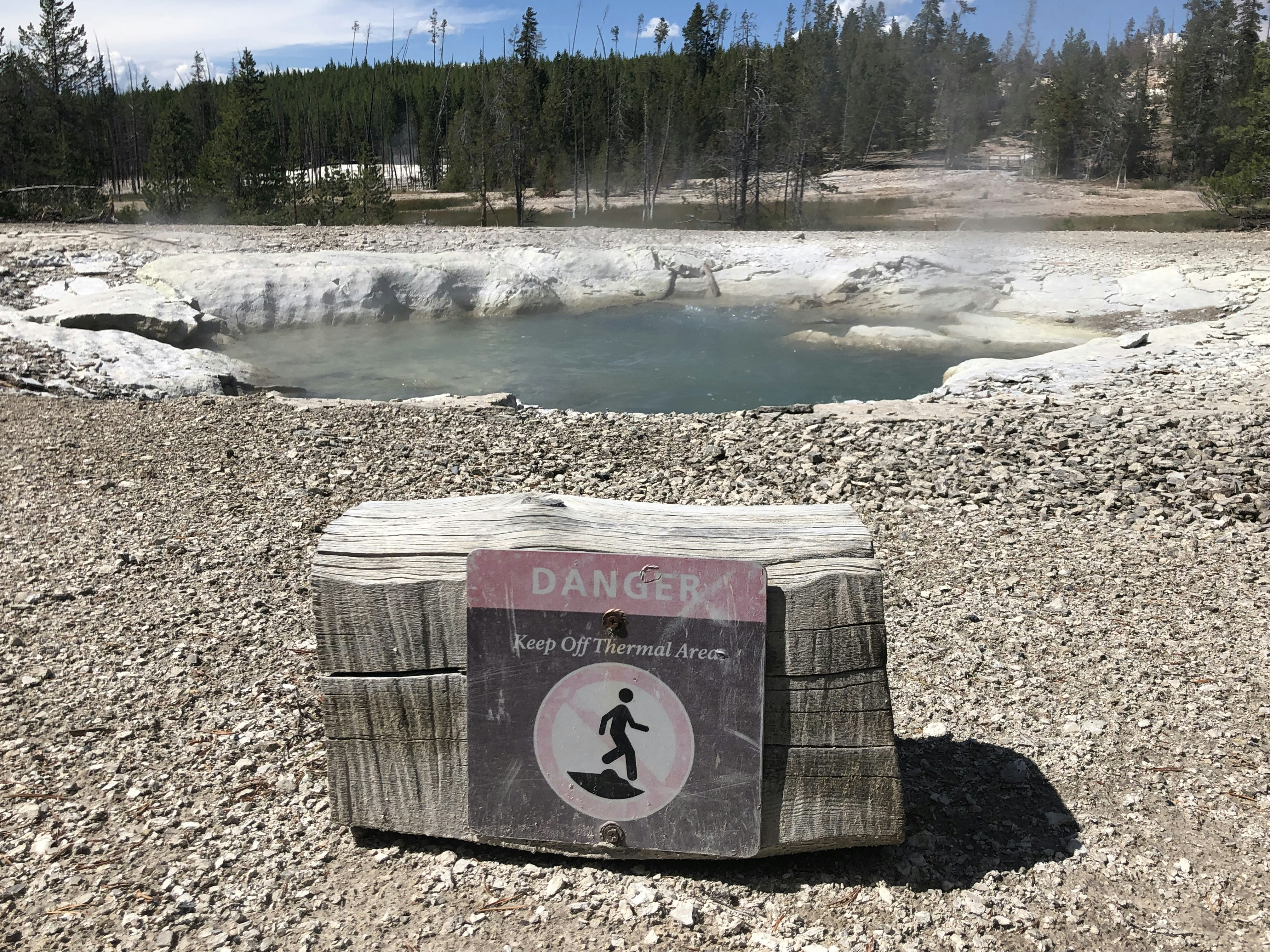 A warning sign advising against venturing into the thermal area is affixed to a large log in Yellowstone National Park