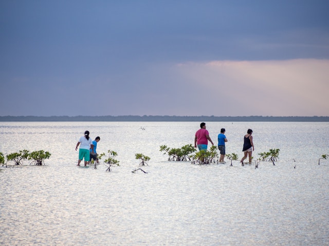 People wade in the shallow sea at sunset at Isla Blanca, near Cancún, Quintana Roo, Mexico