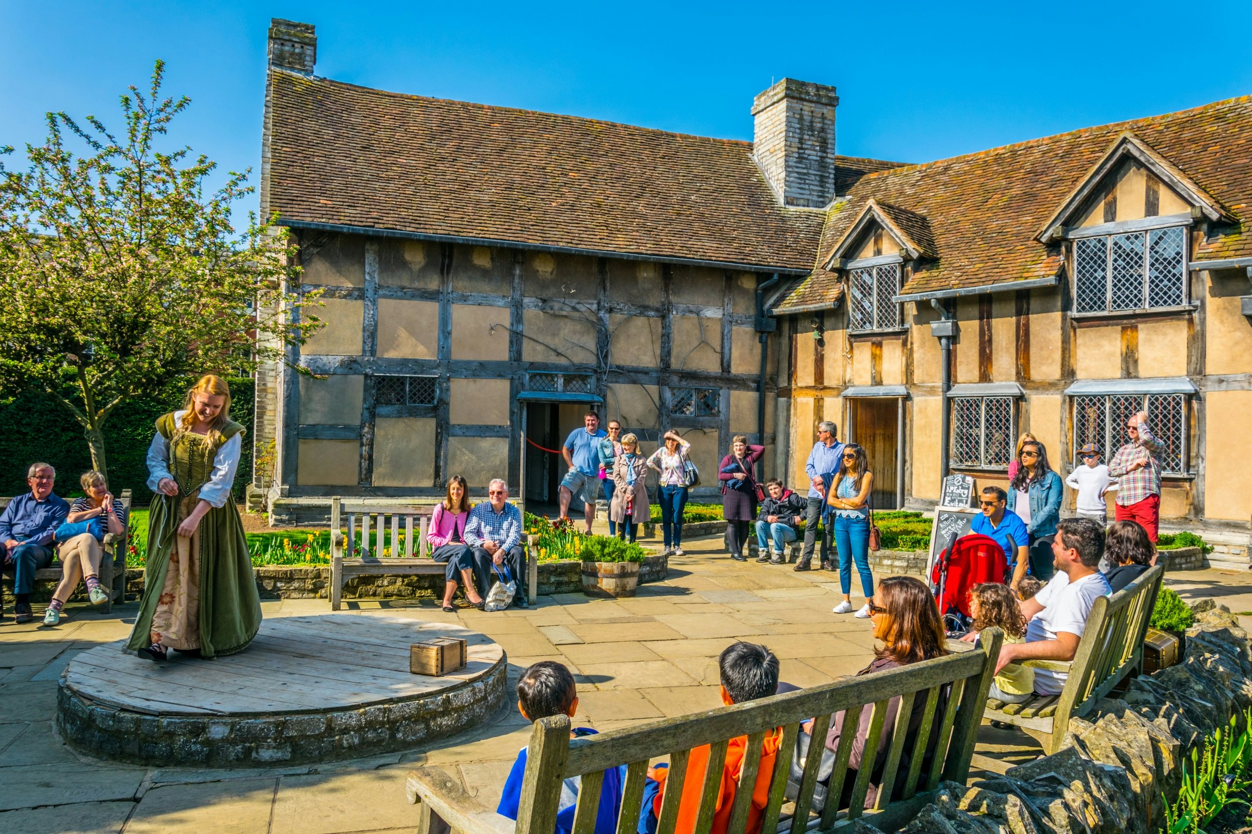 Actors perform to a small crowd outside a Tudor house