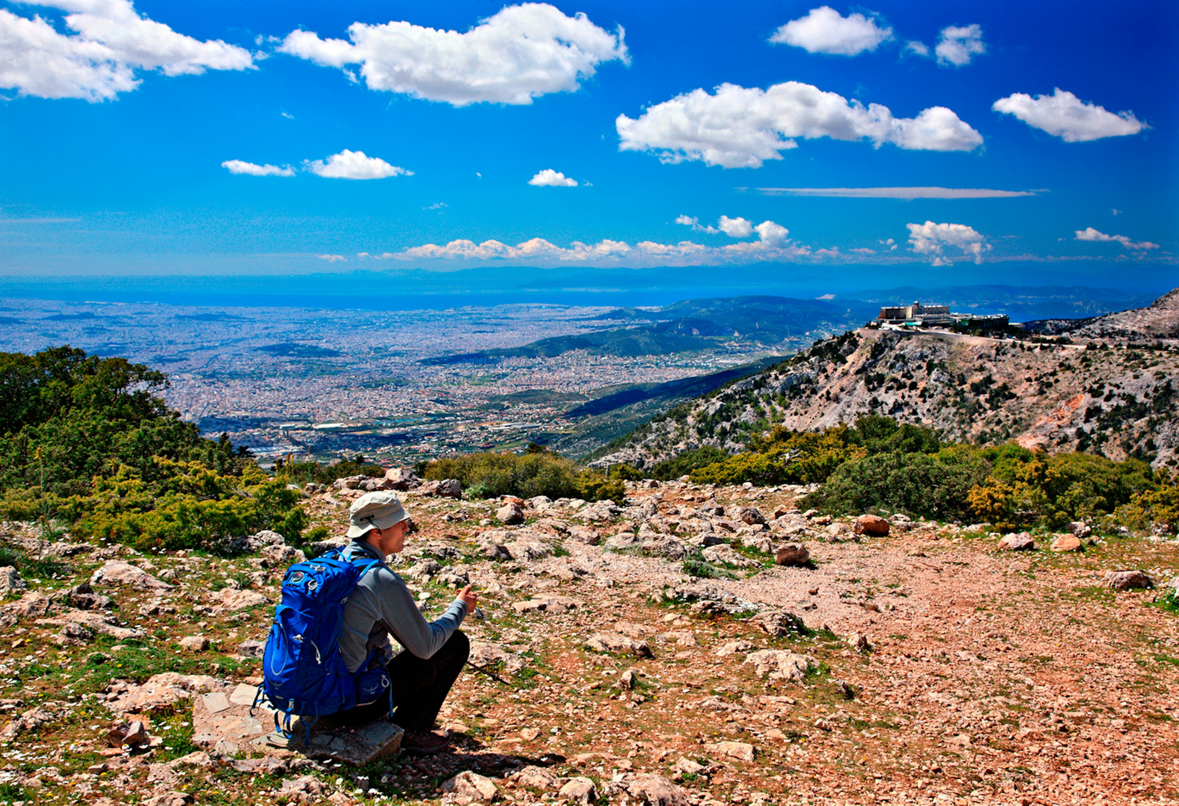 A hiker sits at the top of a mountain gazing out over the view of hills below