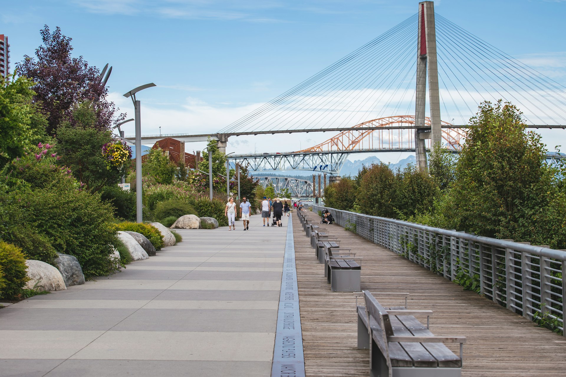 People walk along New Westminster Pier Park with the Port Mann Bridge in the background, New Westminster, British Columbia, Canada