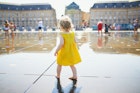 A toddler in a yellow sundress playing in the Miroir d'Eau in Bordeaux