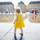 A toddler in a yellow sundress playing in the Miroir d'Eau in Bordeaux