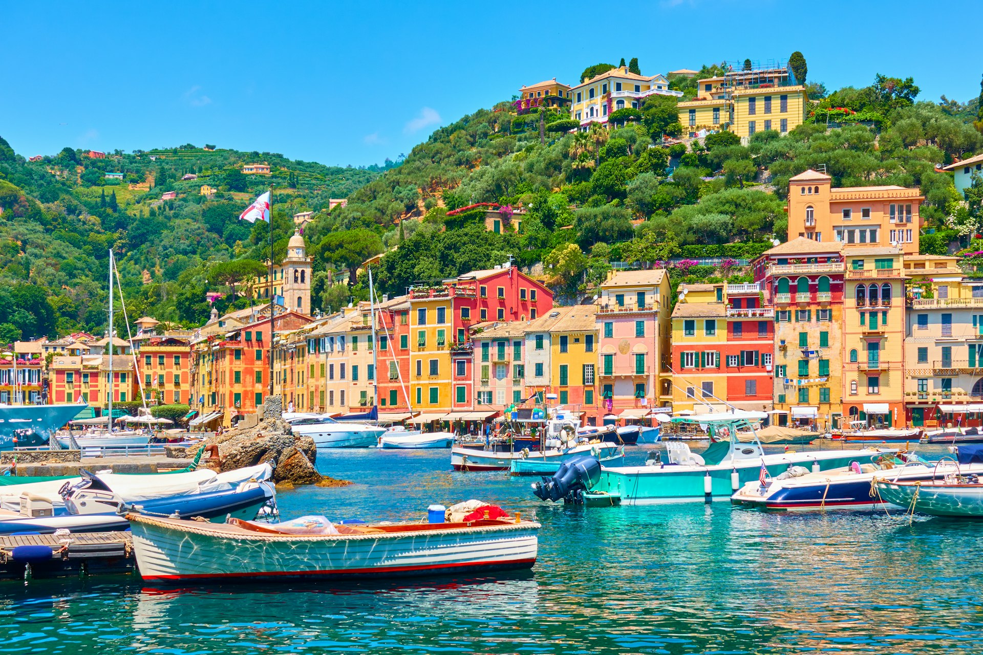 The birhgtly-colored houses dotted around the harbor at Portofino, Italy with boats lapping in the waves in the sun 