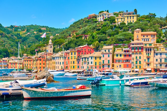 The birhgtly-colored houses dotted around the harbor at Portofino, Italy with boats lapping in the waves in the sun