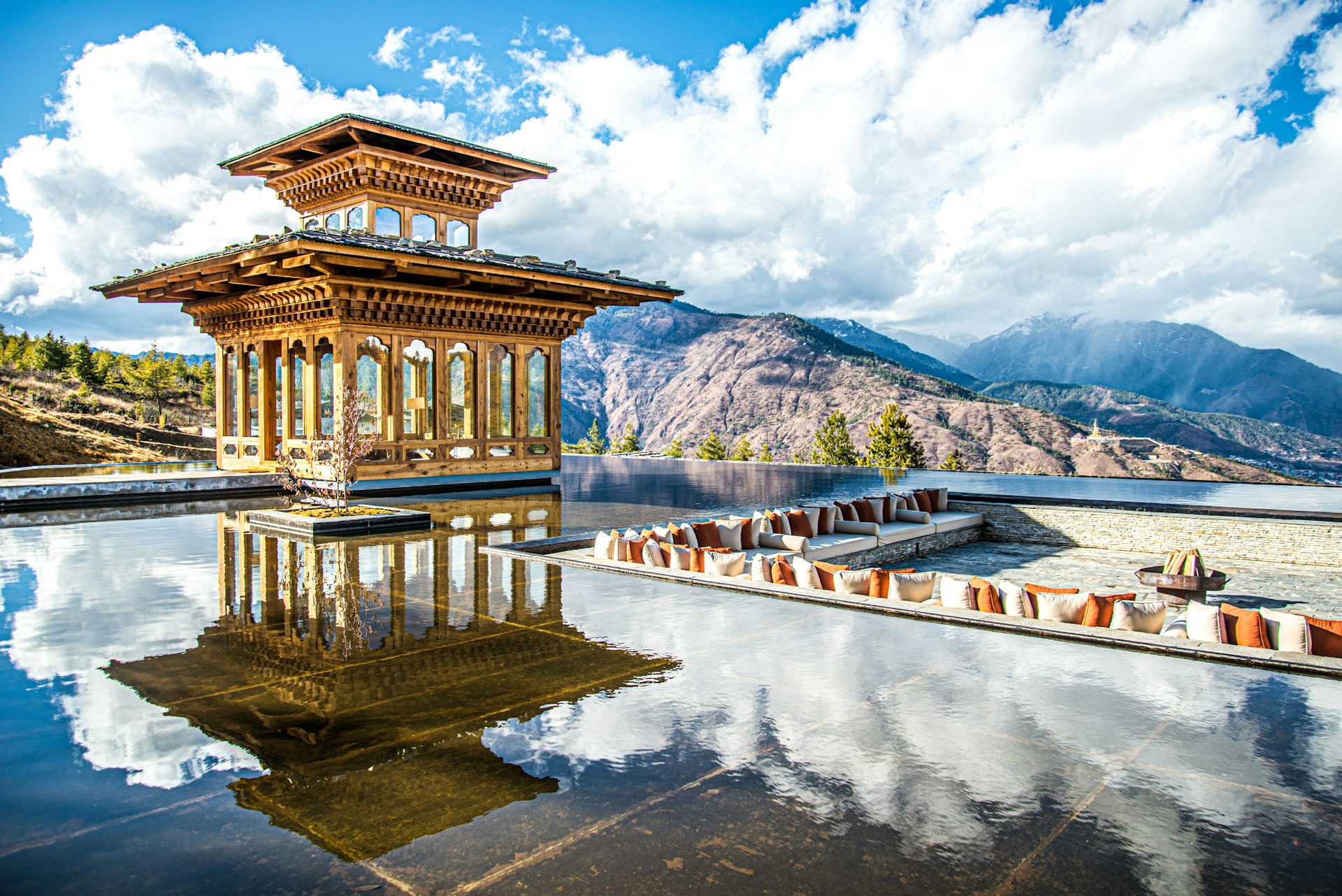 A resting area by a pool in Thimphu, Bhutan, on a bright day, with the clouds overhead reflected in the water. 