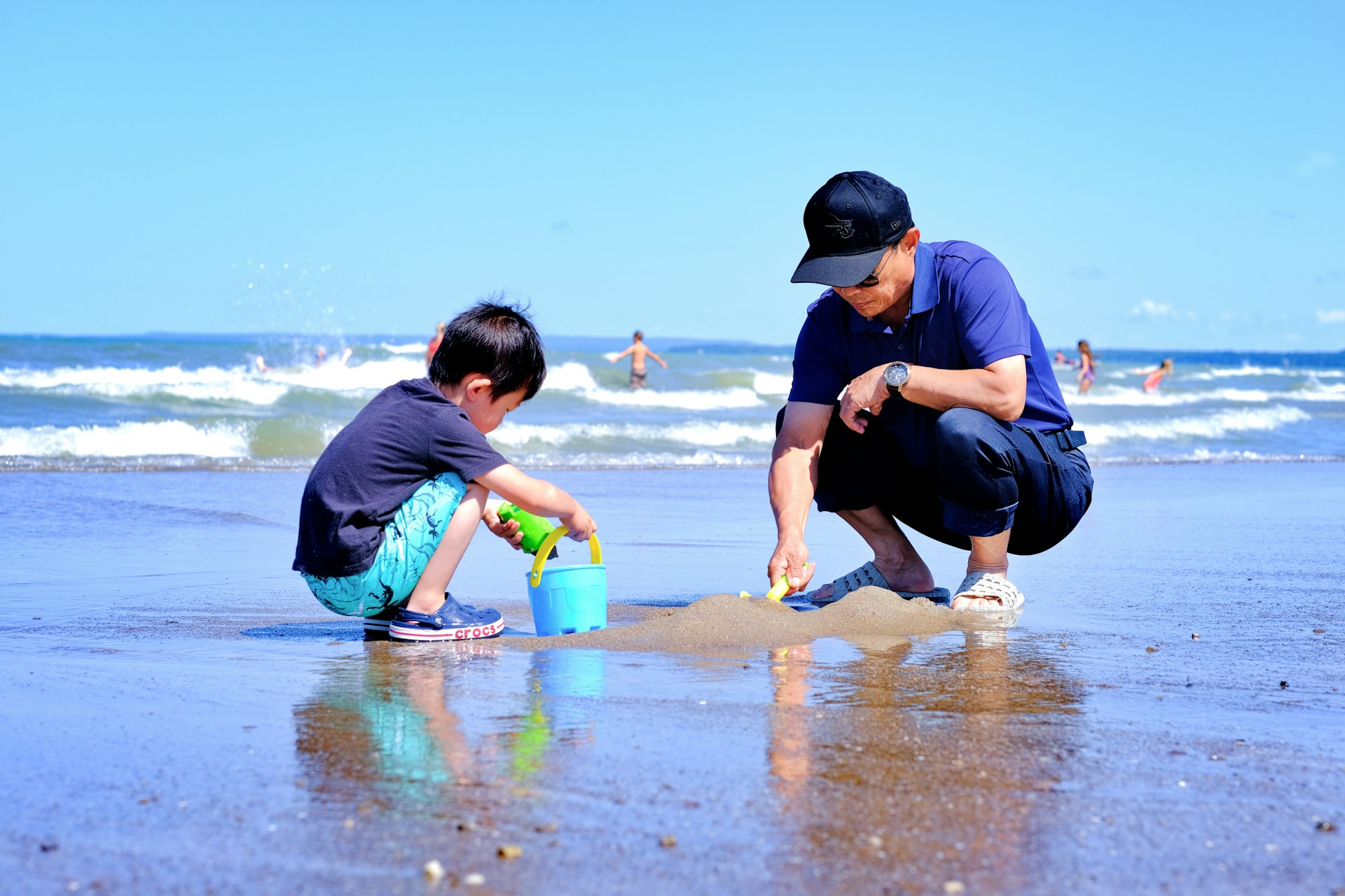 A grandpa plays on a sandy beach with his grandson 