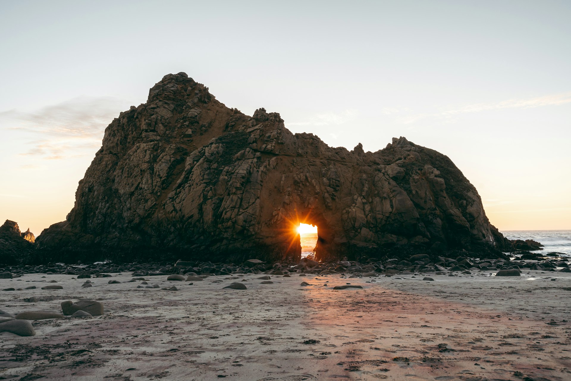 A luz do pôr do sol passa pelo arco de uma formação rochosa, Pfeiffer Beach, Big Sur, Califórnia