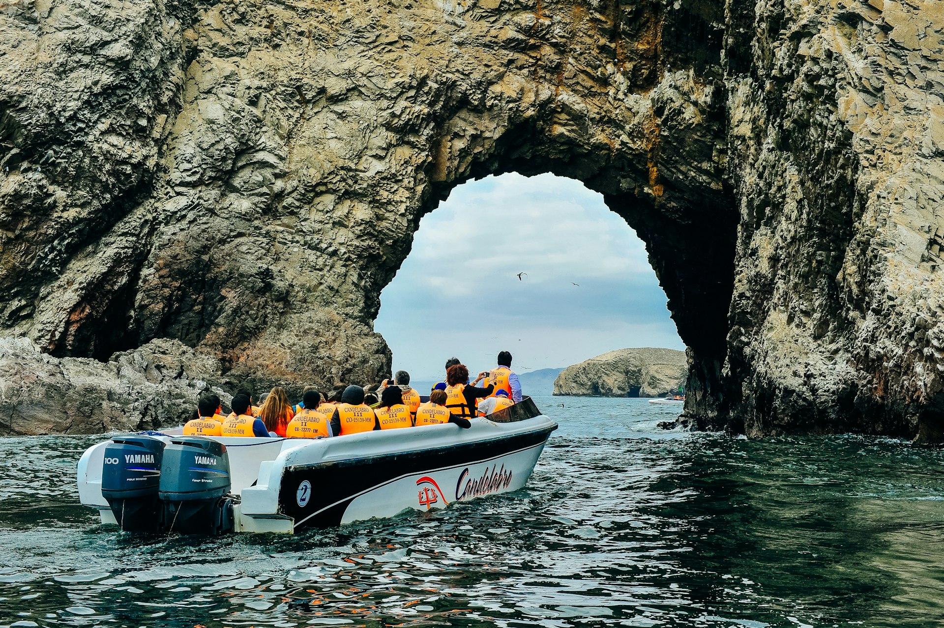 People wearing safety vests sit in a boat that is touring an island