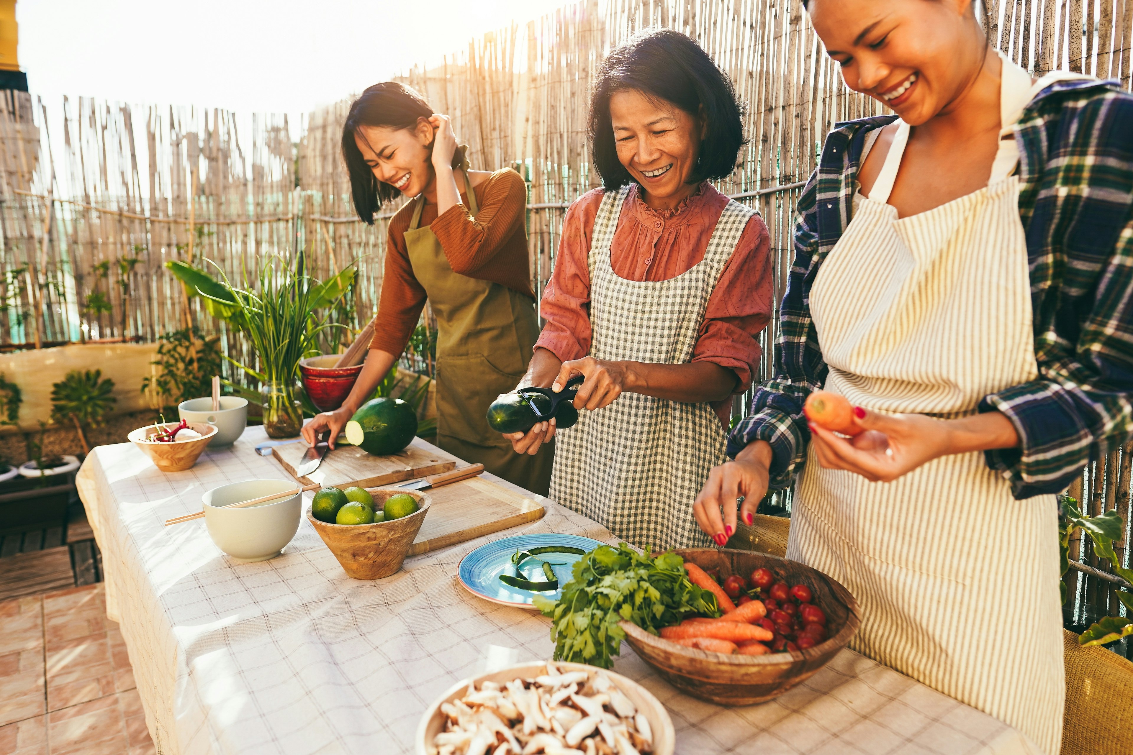 Three people prepare food together at a long bench