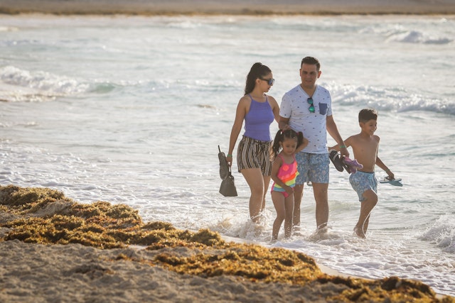 A family walks along the beach past the seaweed at Playa Forum, Cancún, Quintana Roo, Mexico