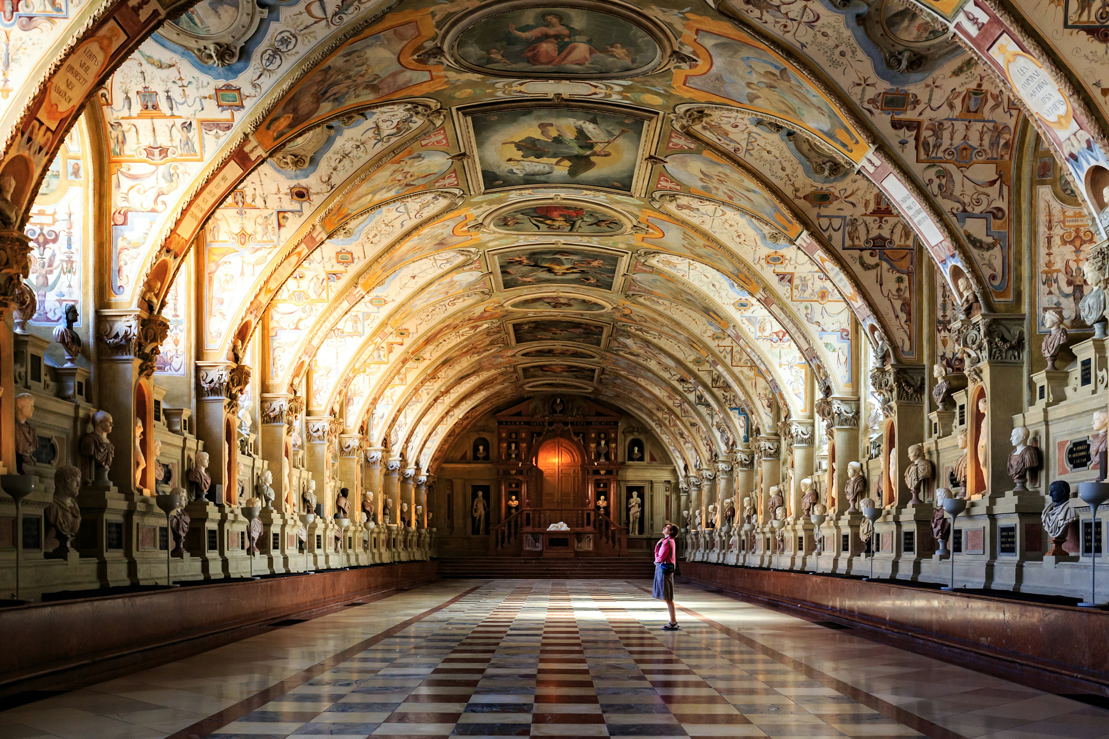 A woman stands in a room admiring the arched, heavlily decorated ceiling