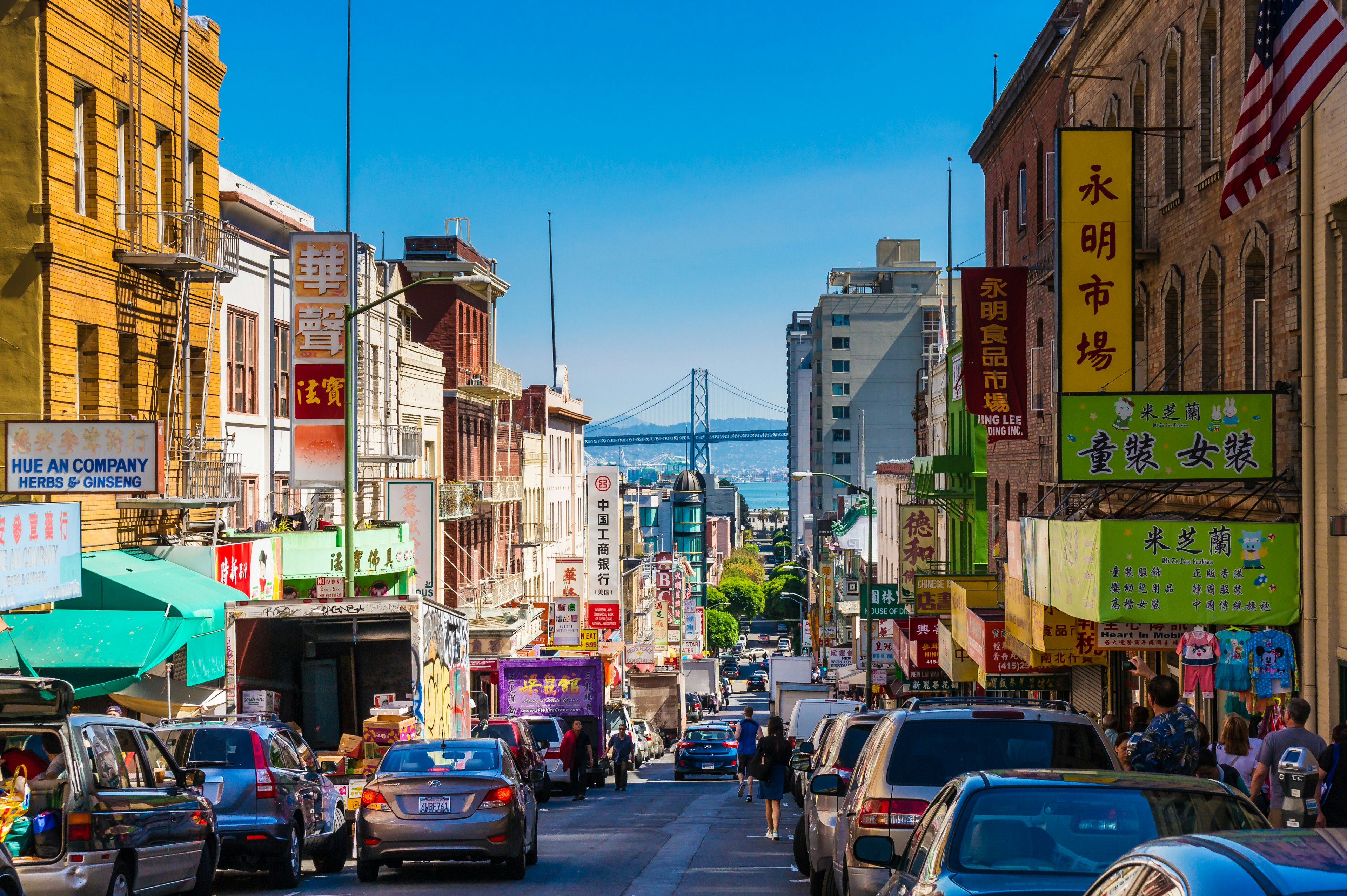 Downtown city life in a busy street of Chinatown, San Francisco. The view has many people, shops and cars and is a lookout to the Oakland Bay Bridge.