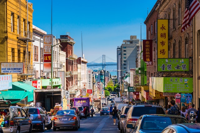 Downtown city life in a busy street of Chinatown, San Francisco. The view has many people, shops and cars and is a lookout to the Oakland Bay Bridge.