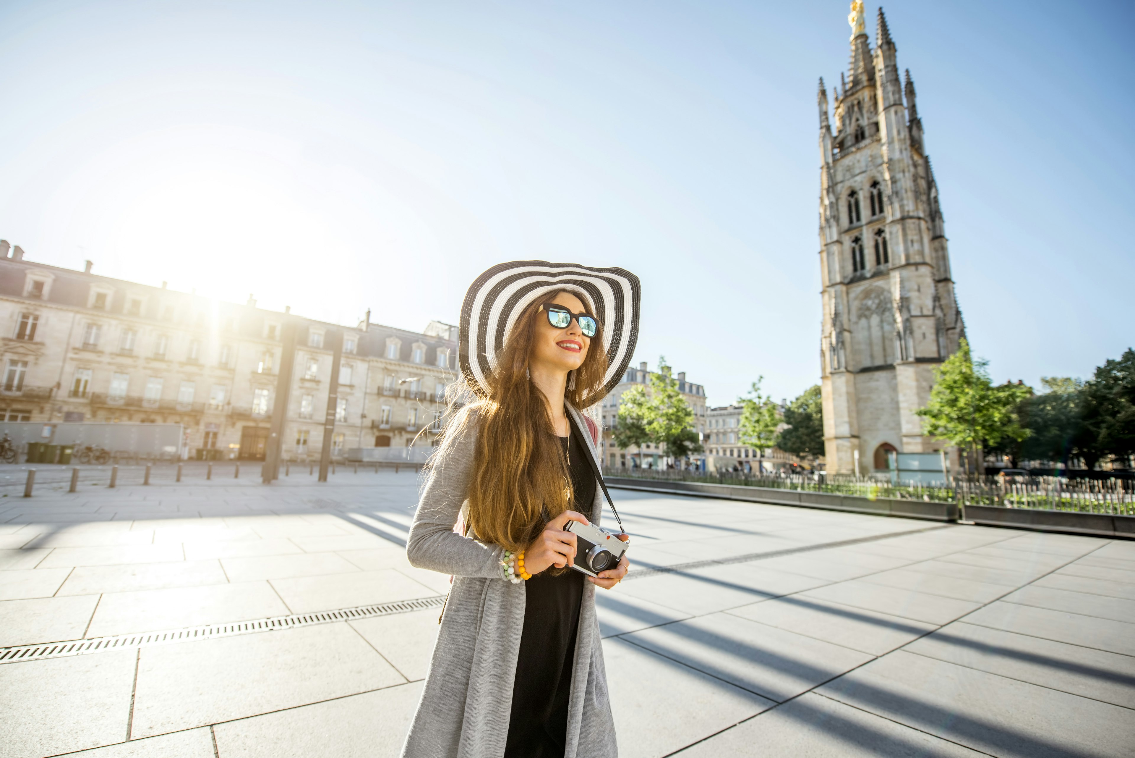 Young woman tourist walking with a camera on the Pey-Berland square with the bell tower in the background in Bordeaux