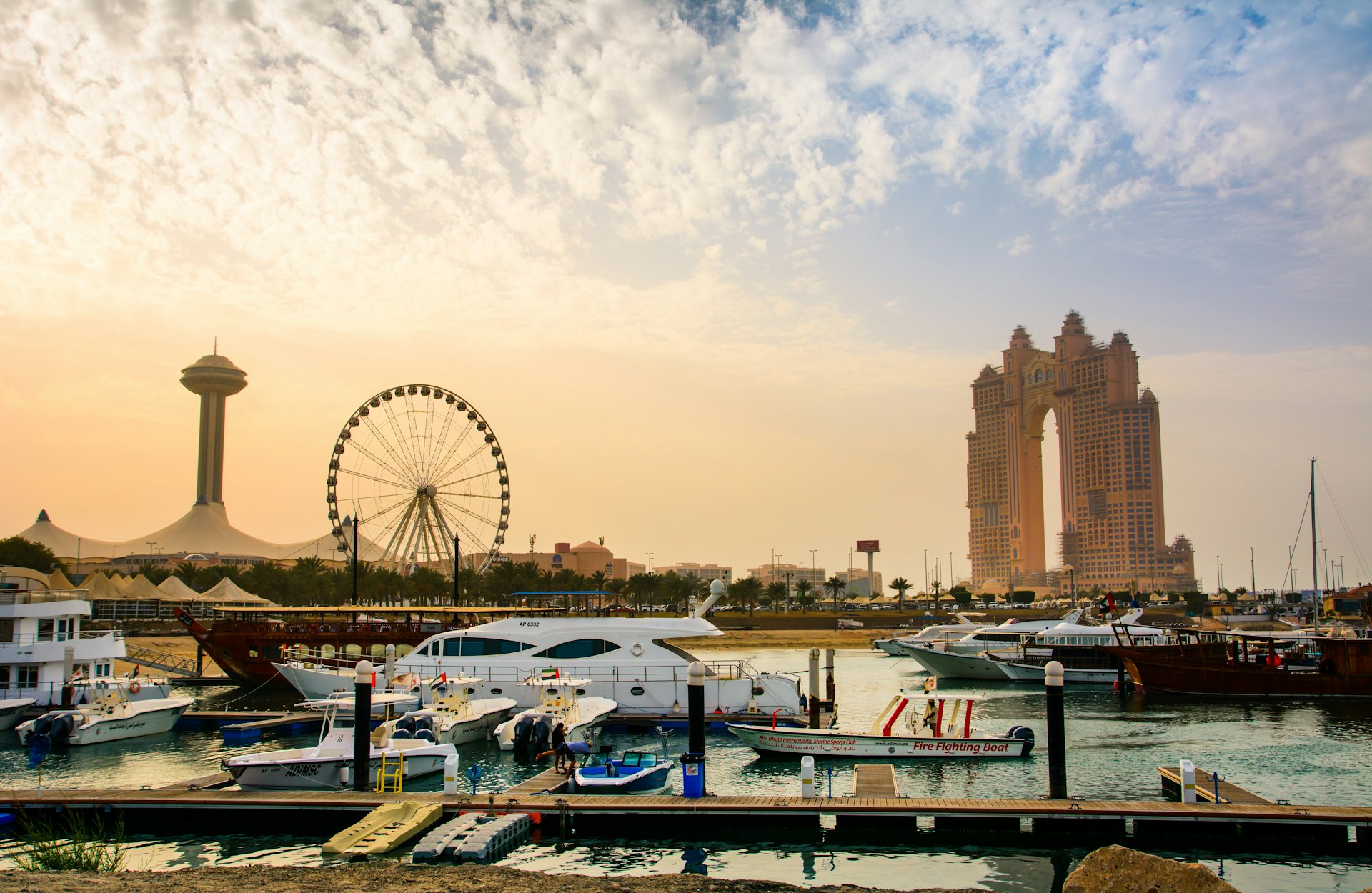 Sunset over an island with a Ferris wheel, large hotel and luxury boats in the dock