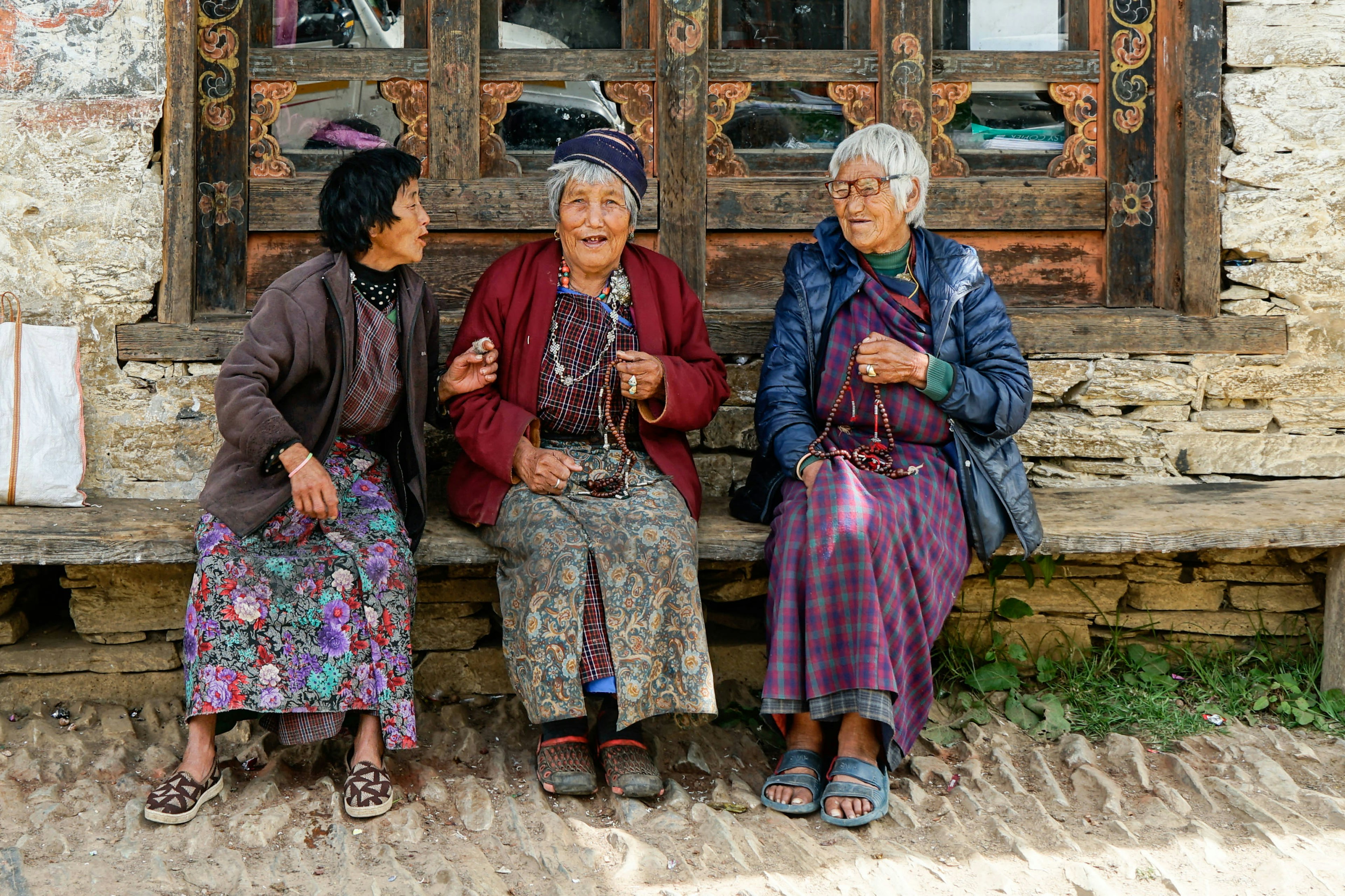 Three women sitting in front of a traditional house in Mongar, Bhutan.