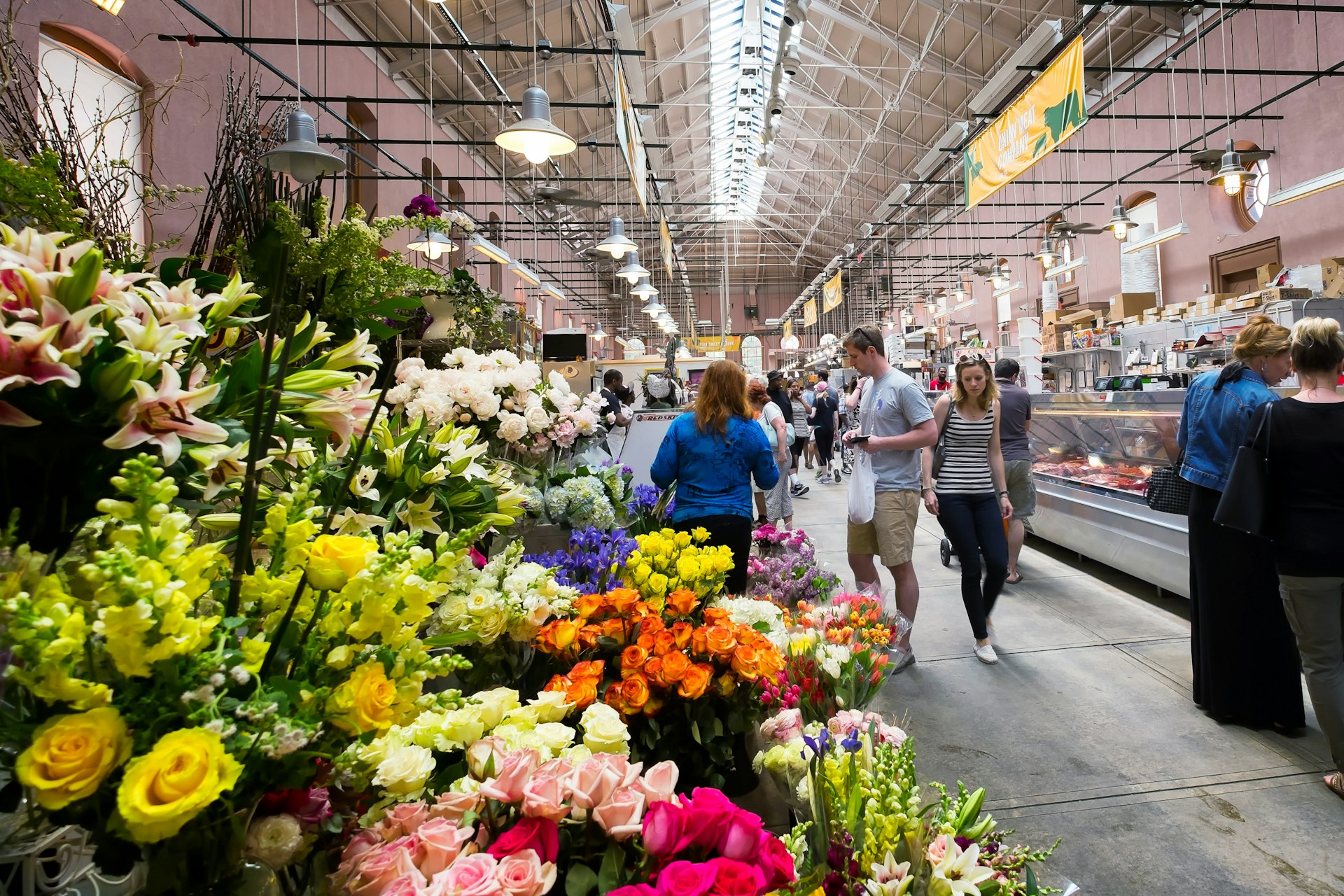 A market with fresh flowers on display on one side of the hall and meat counters on the other