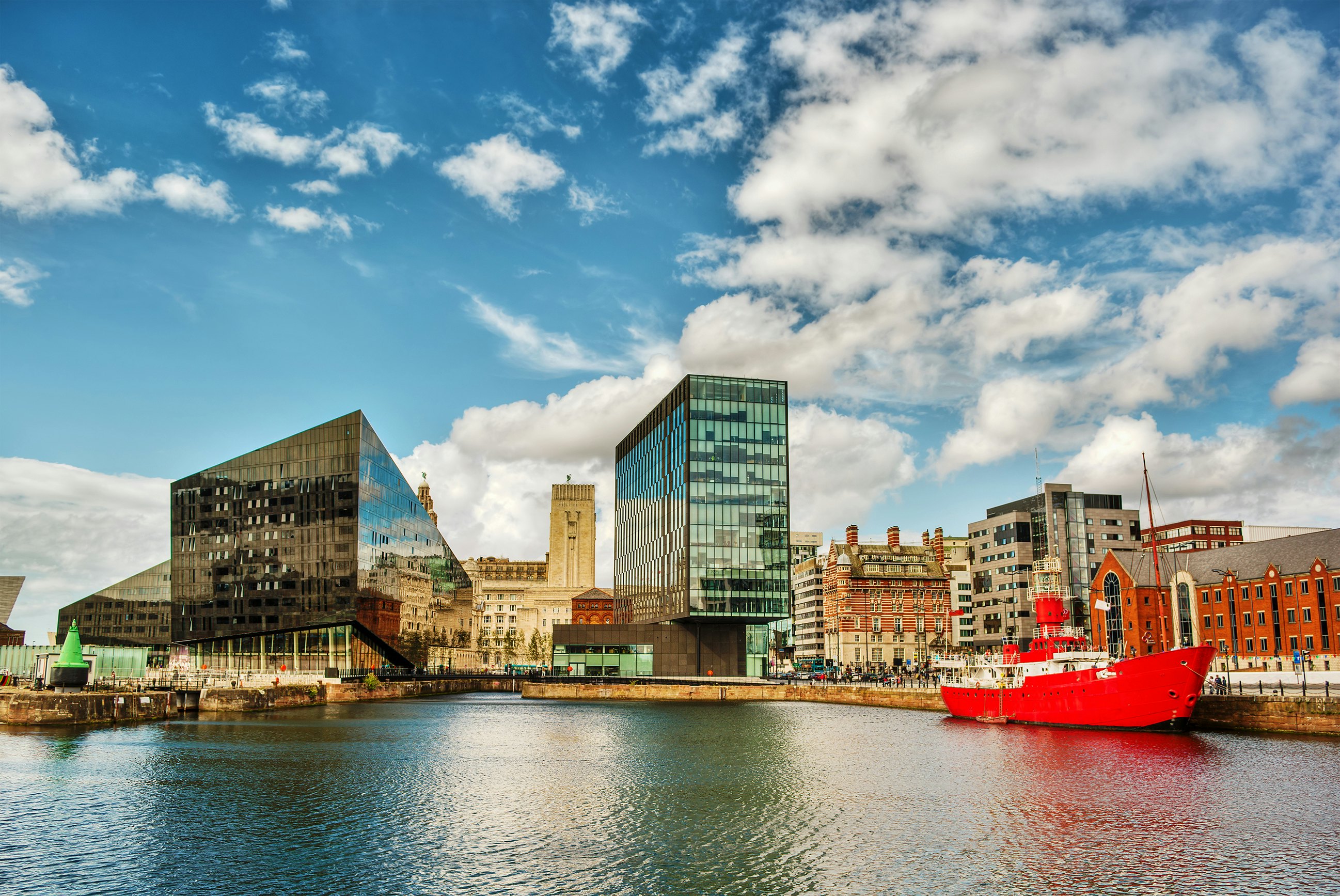 Modern and restored historic buildings along the edge of a dock with a large red boat moored nearby