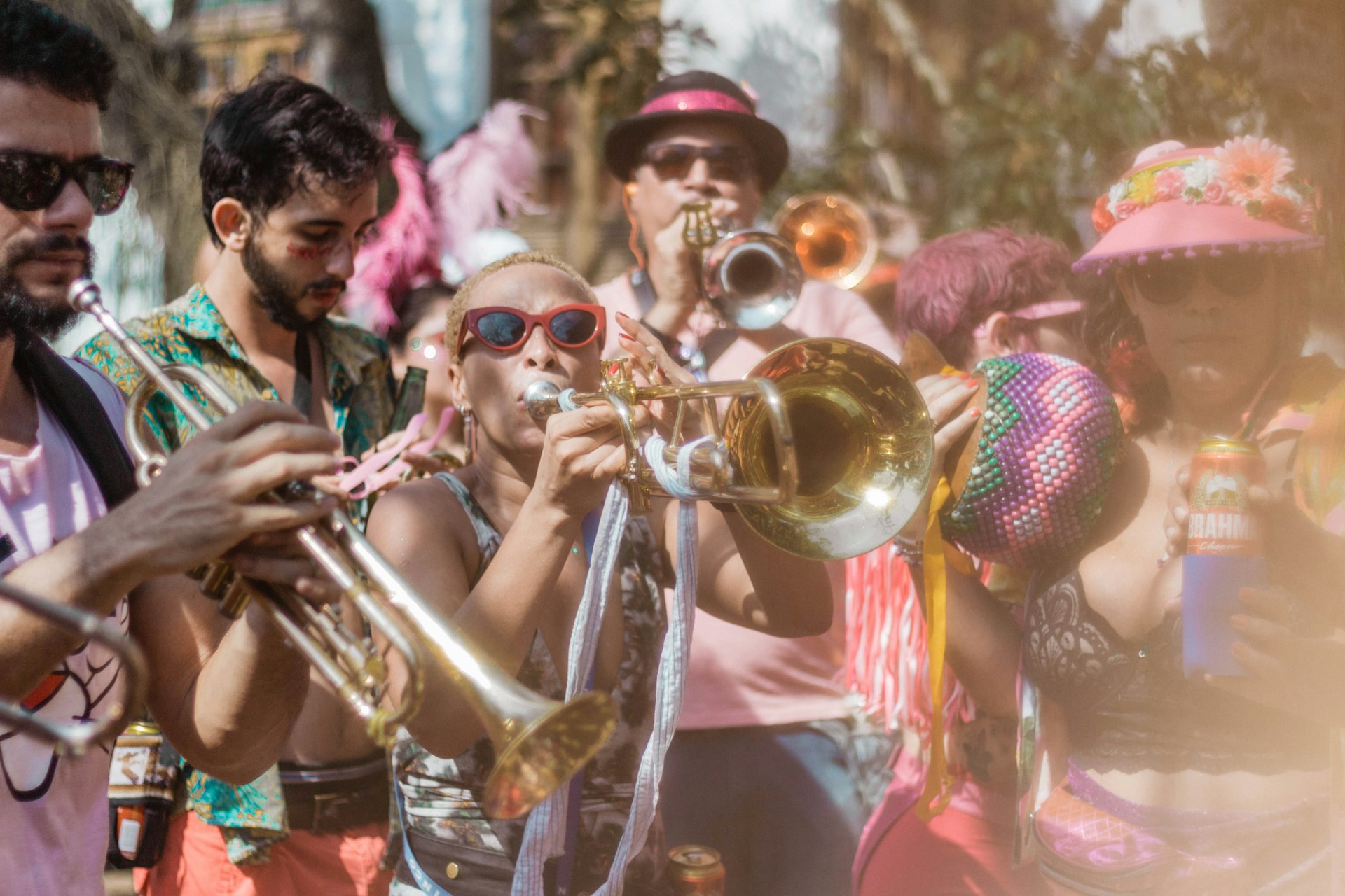 Musicians playing brass instruments on a sunny day, with a hazy effect giving a dreamy quality to a street carnival scene filled with colorful attire.