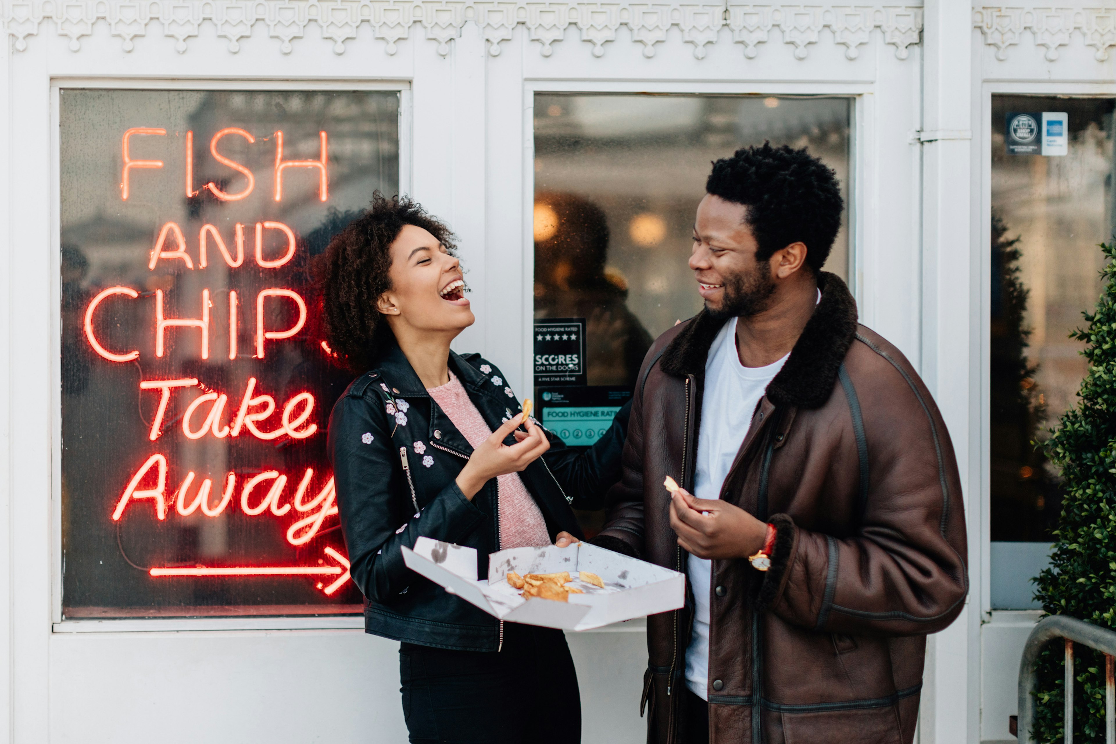 Mixed race couple on a day out at seaside having fun and laughing outside a fish and chip shop