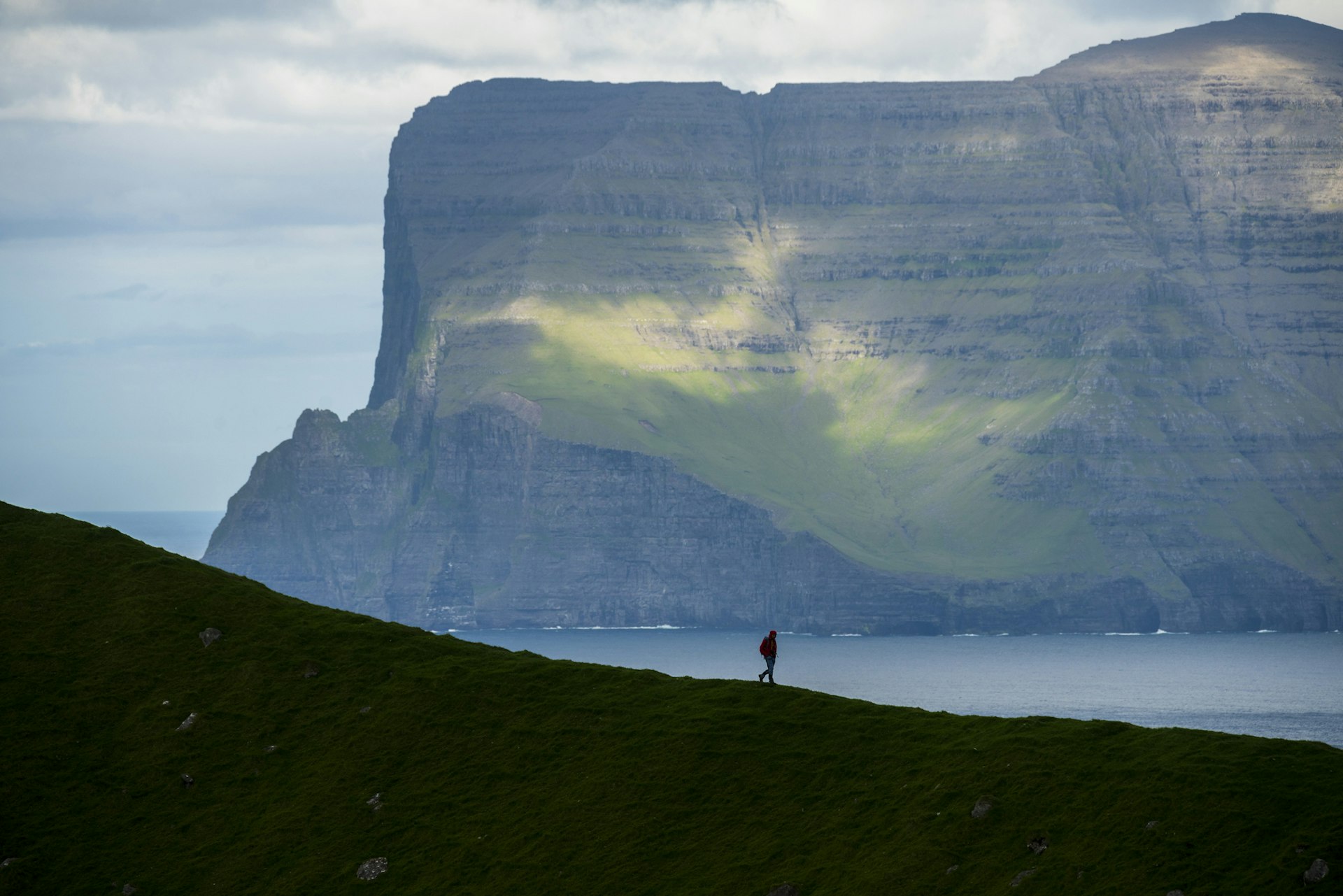 A hiker on a mountain ridge looks towards majestic cliffs 